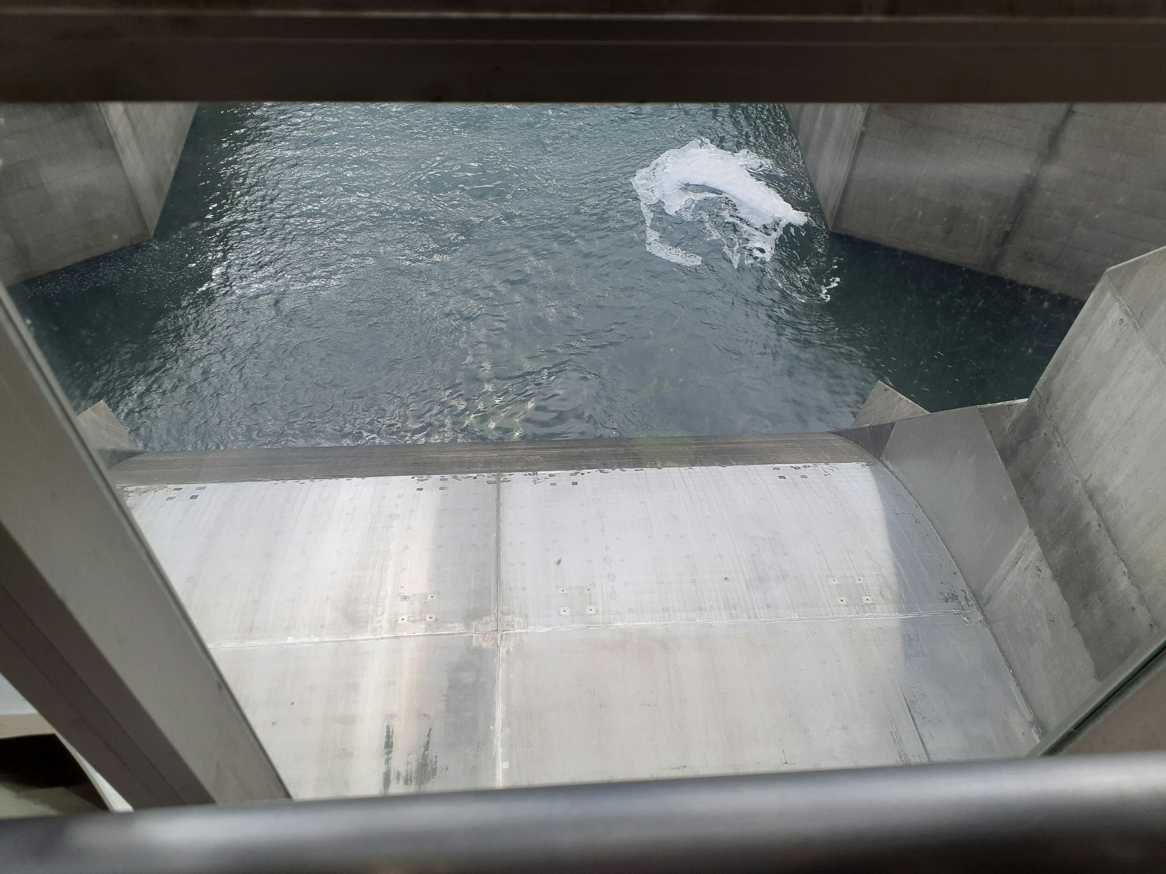 Vista desde el interior de una presa mostrando agua fluyendo y estructura de concreto