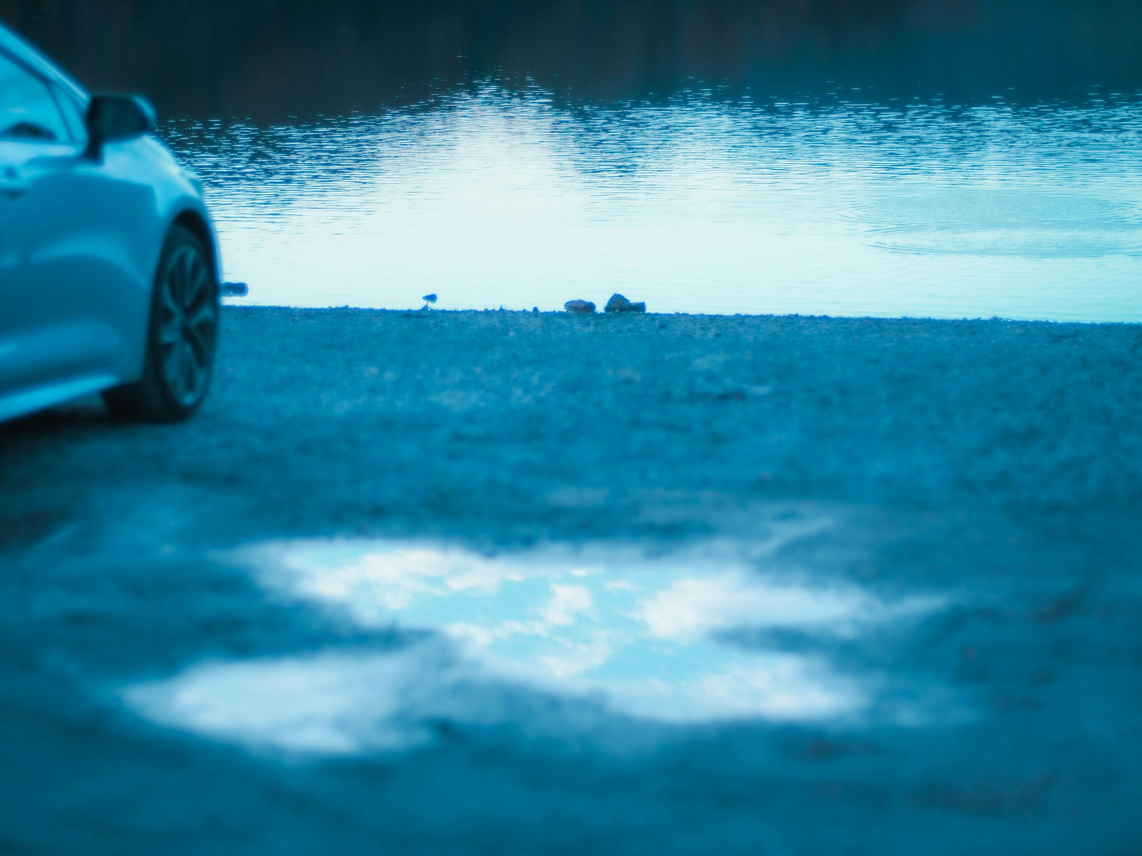 A parked car near a tranquil lake with reflections on the water surface