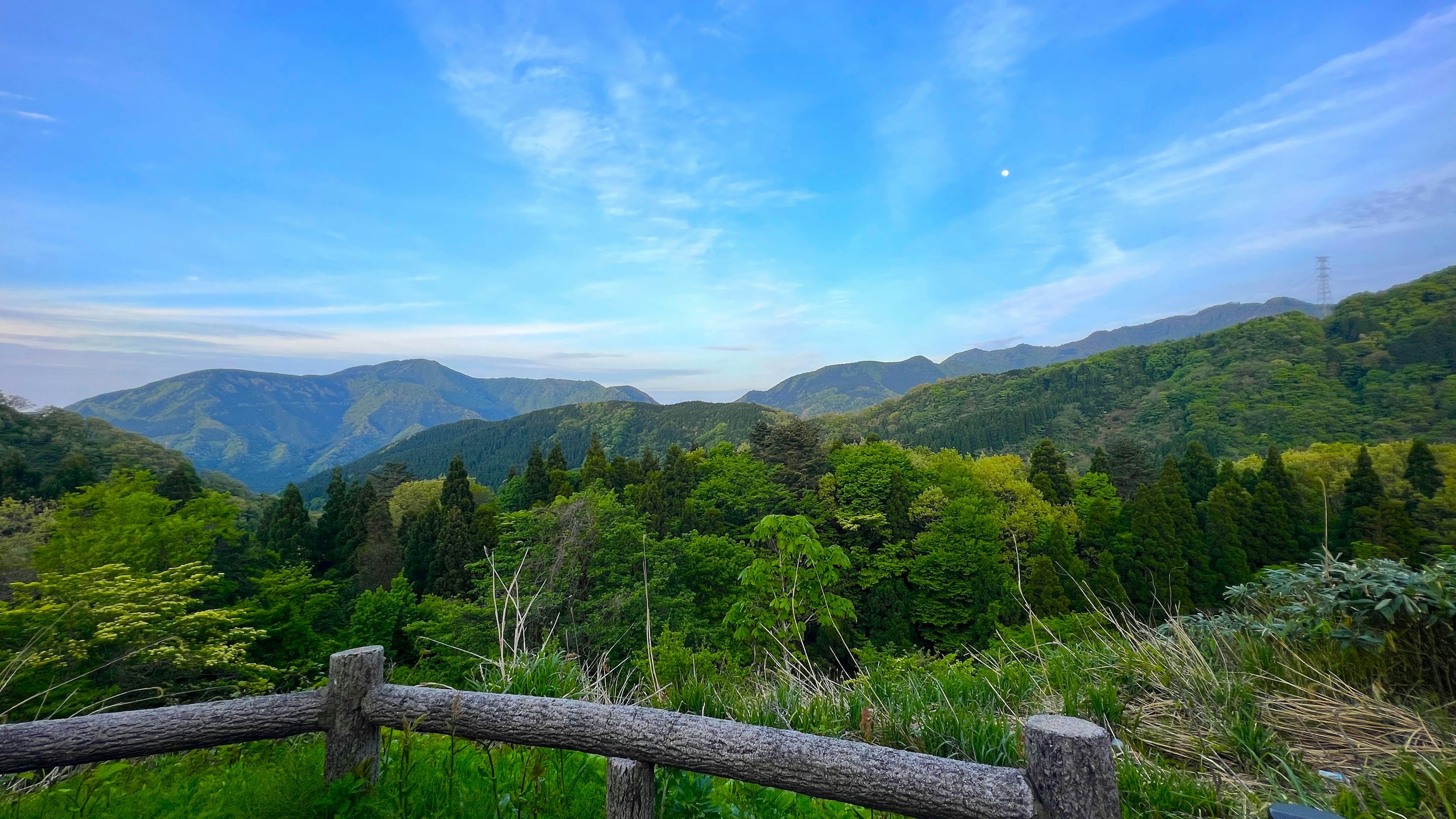 Panoramablick auf grüne Berge unter einem blauen Himmel von einem Aussichtspunkt mit einem Holzzaun