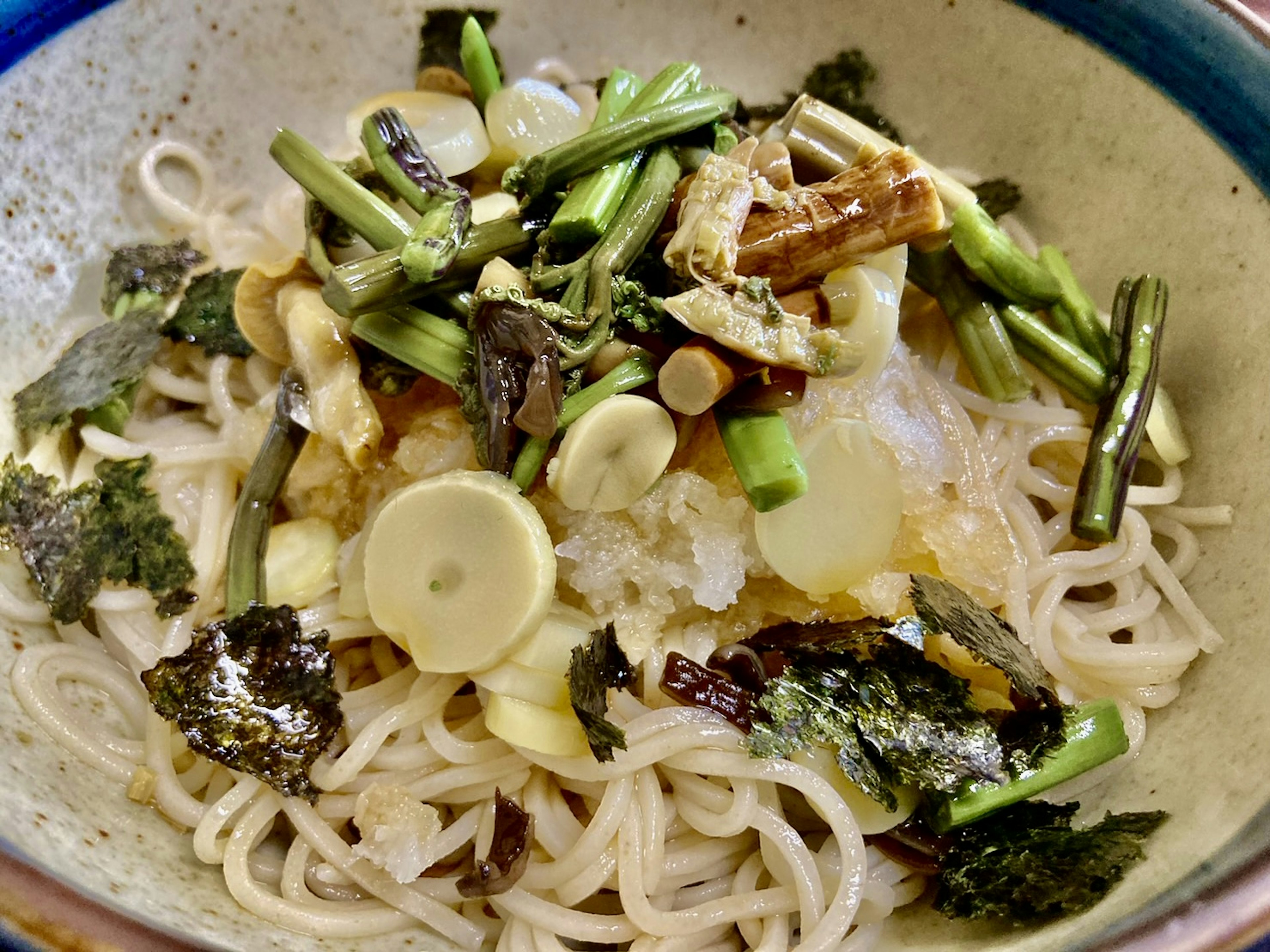 Dish of thin noodles topped with green vegetables and seaweed