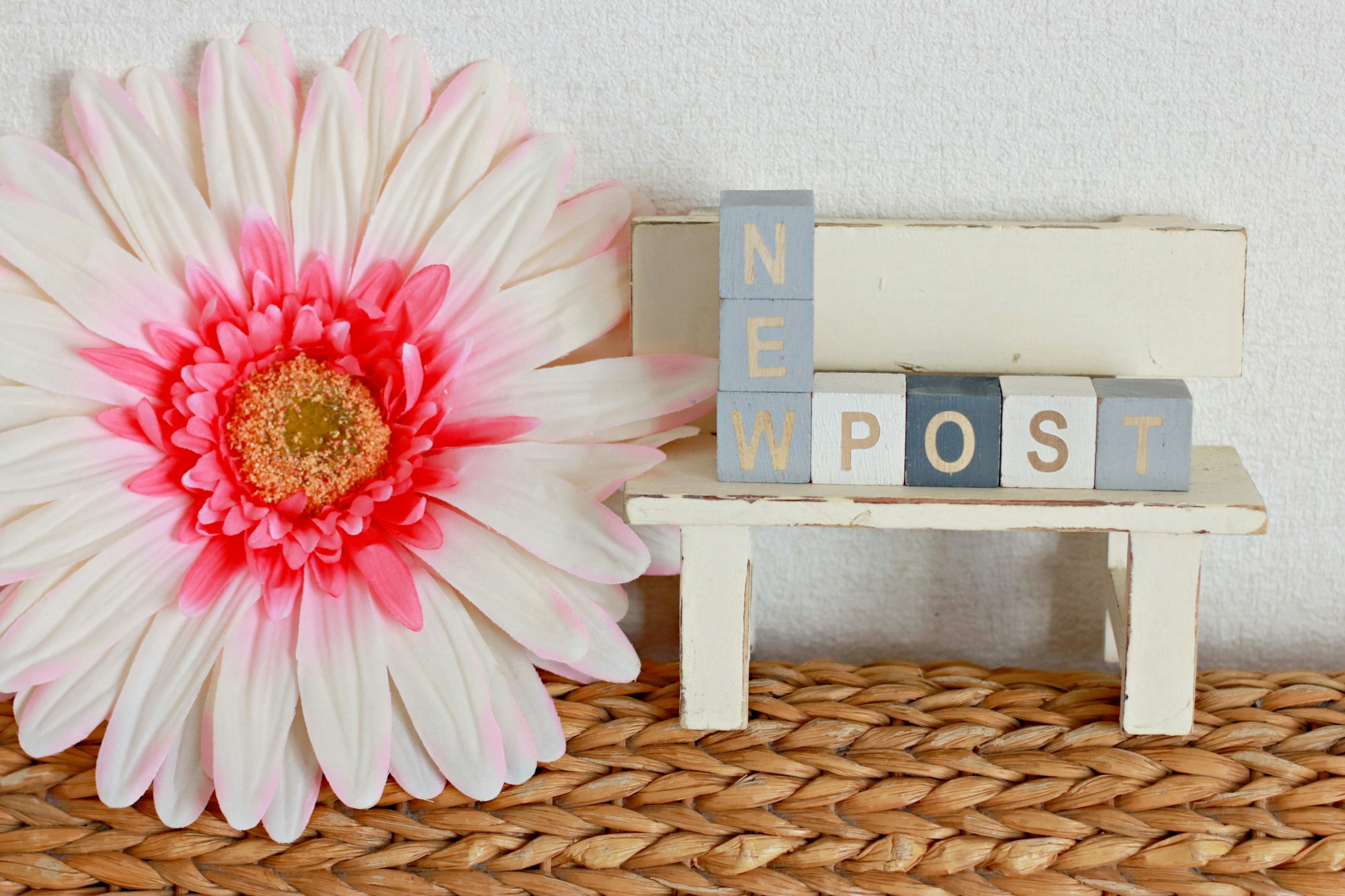 Una panchina bianca con lettere cubiche che spellano 'NEW POST' e un grande fiore rosa