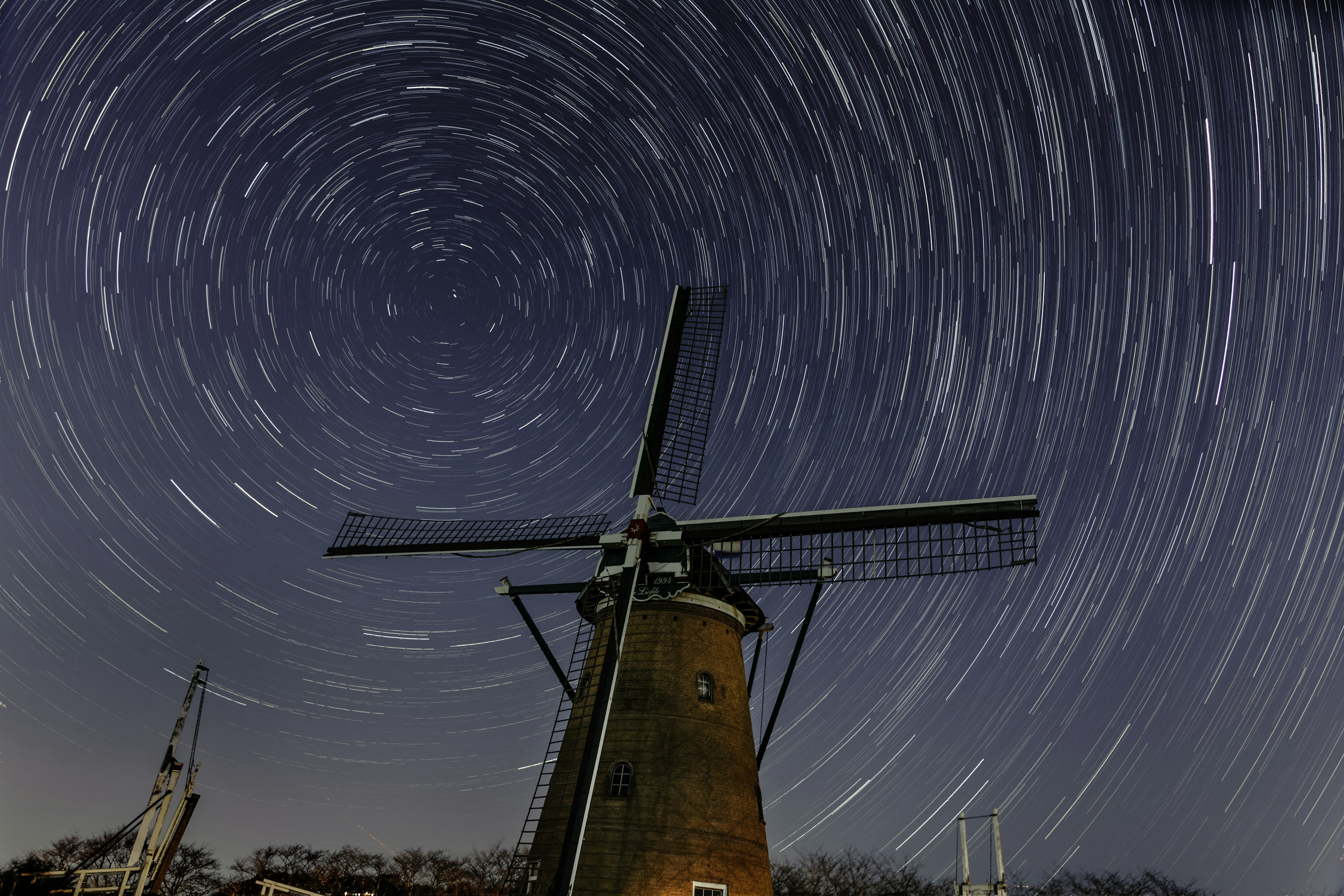 星の軌跡が描かれた夜空の下に立つ風車の風景