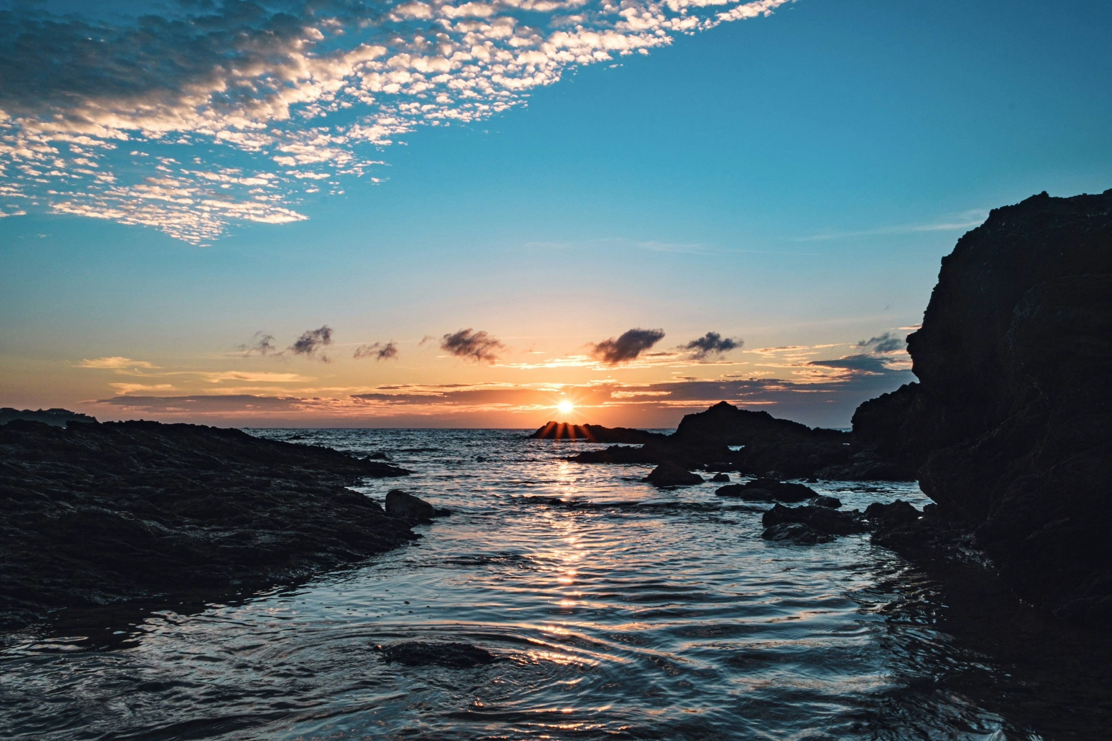 Coastal scene with rocks and sunset reflecting on calm waves