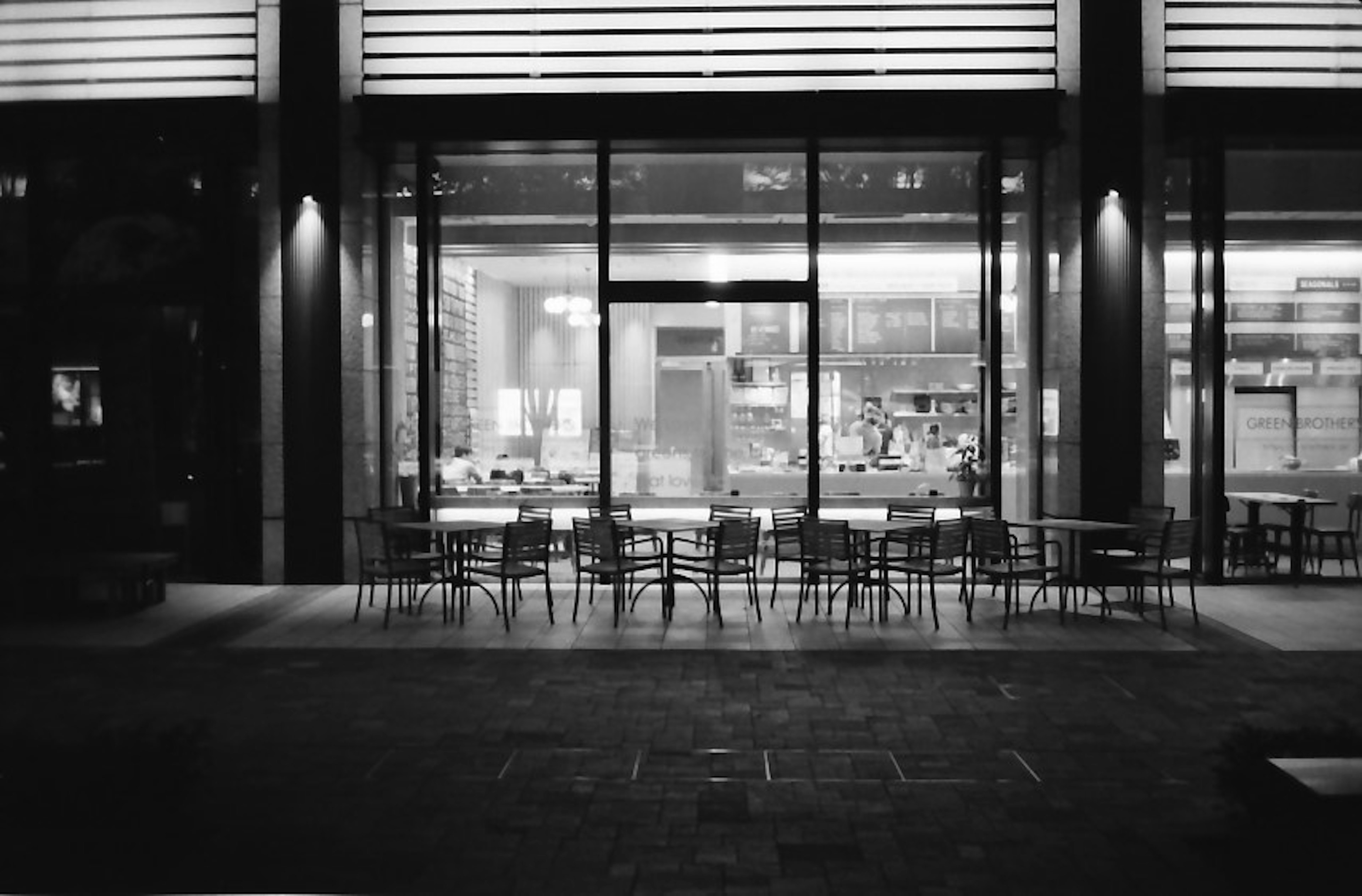 Exterior view of a cafe at night with tables arranged