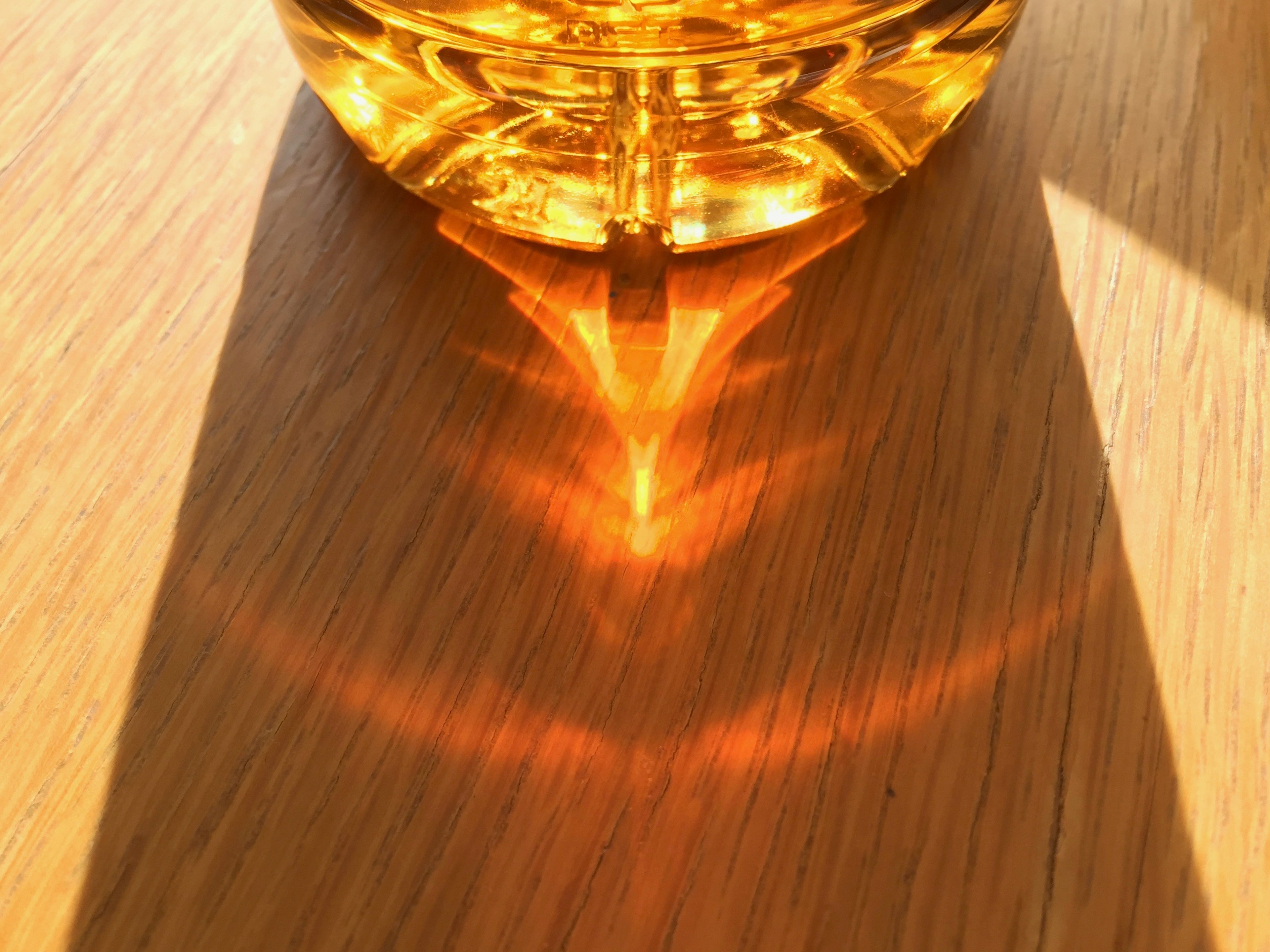 Reflexion von orangefarbenem Licht von einer transparenten Flasche auf einem Holztisch