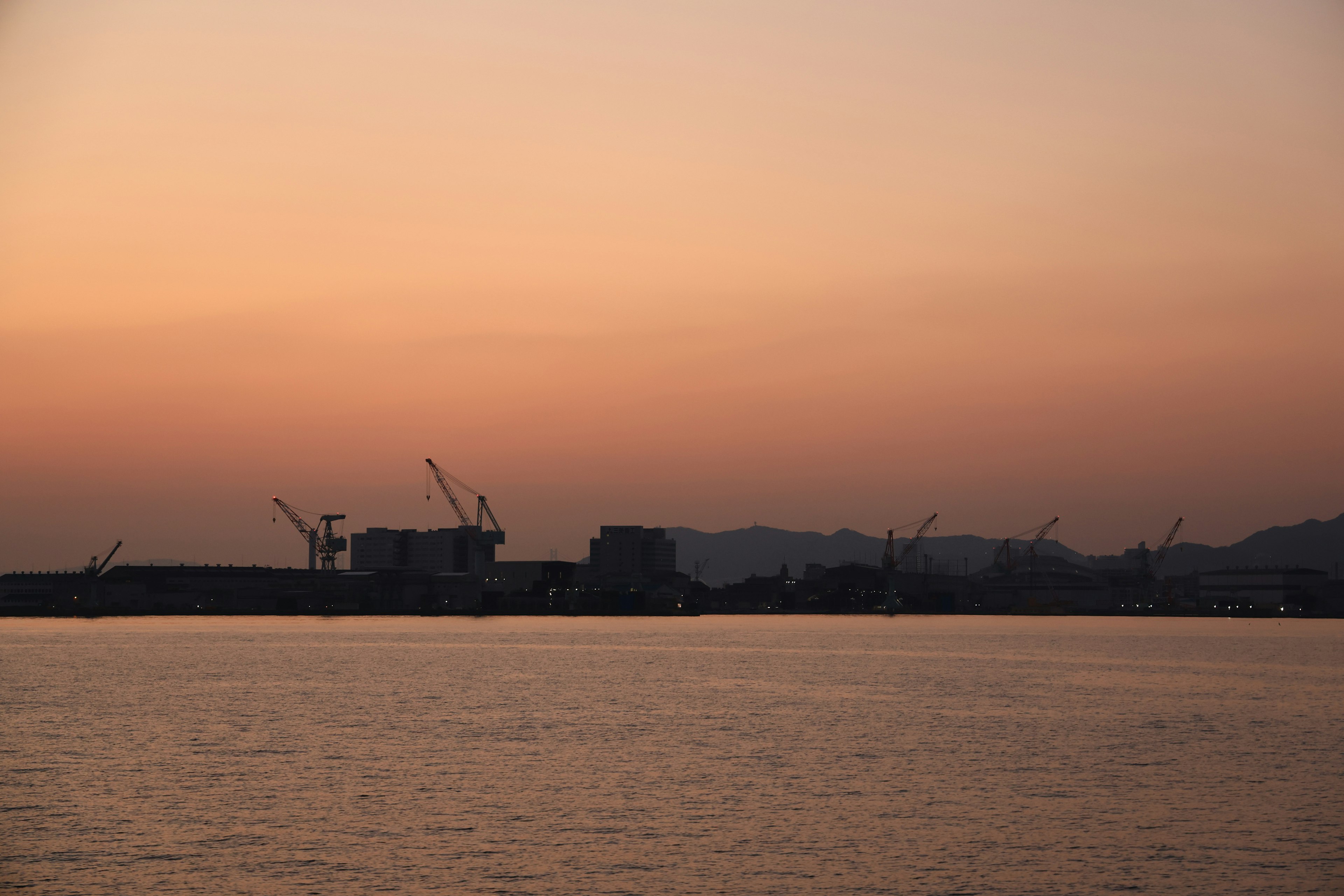 Sonnenuntergang über einem Hafen mit silhouettierten Kränen