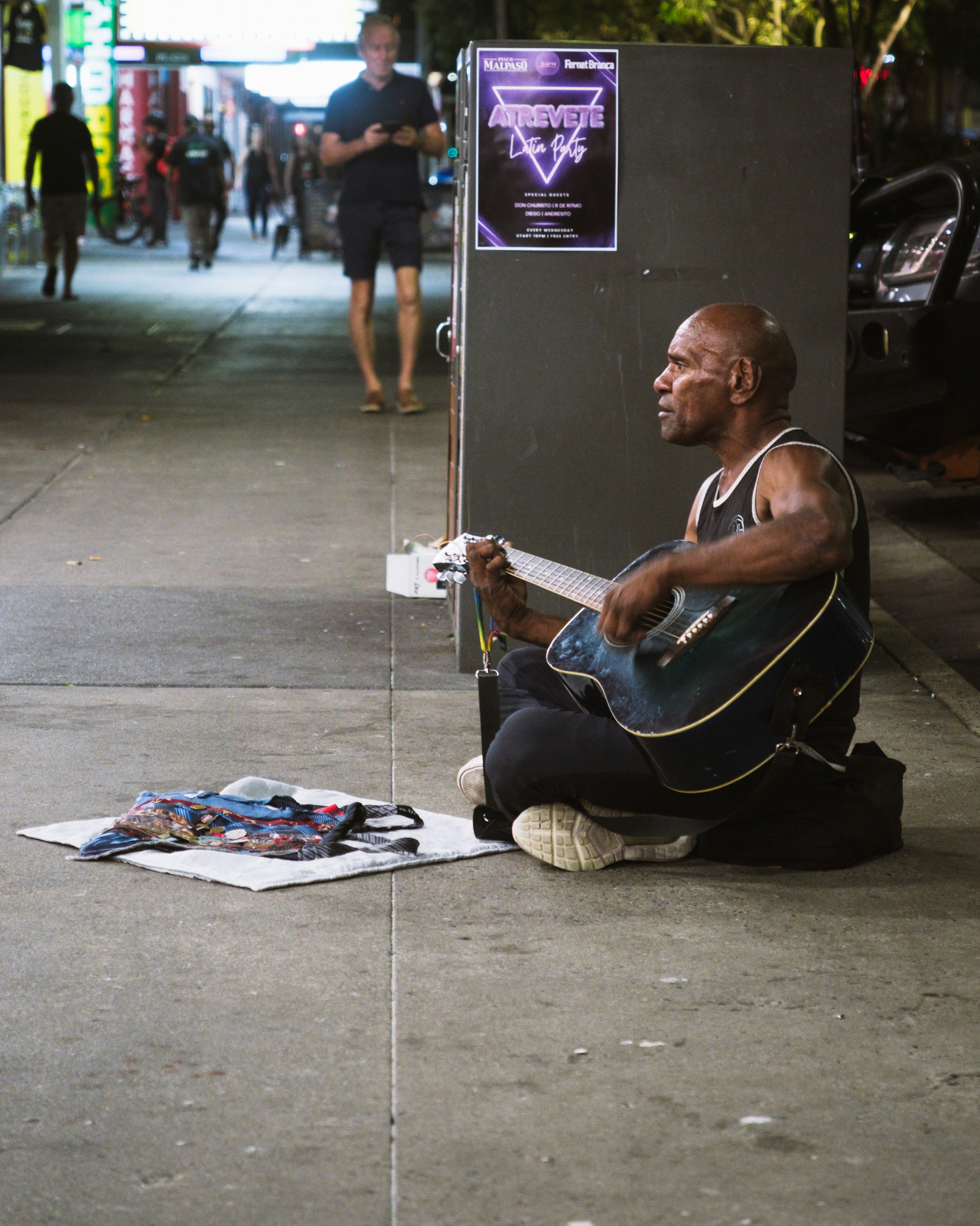 A man playing guitar on the street sitting on the ground