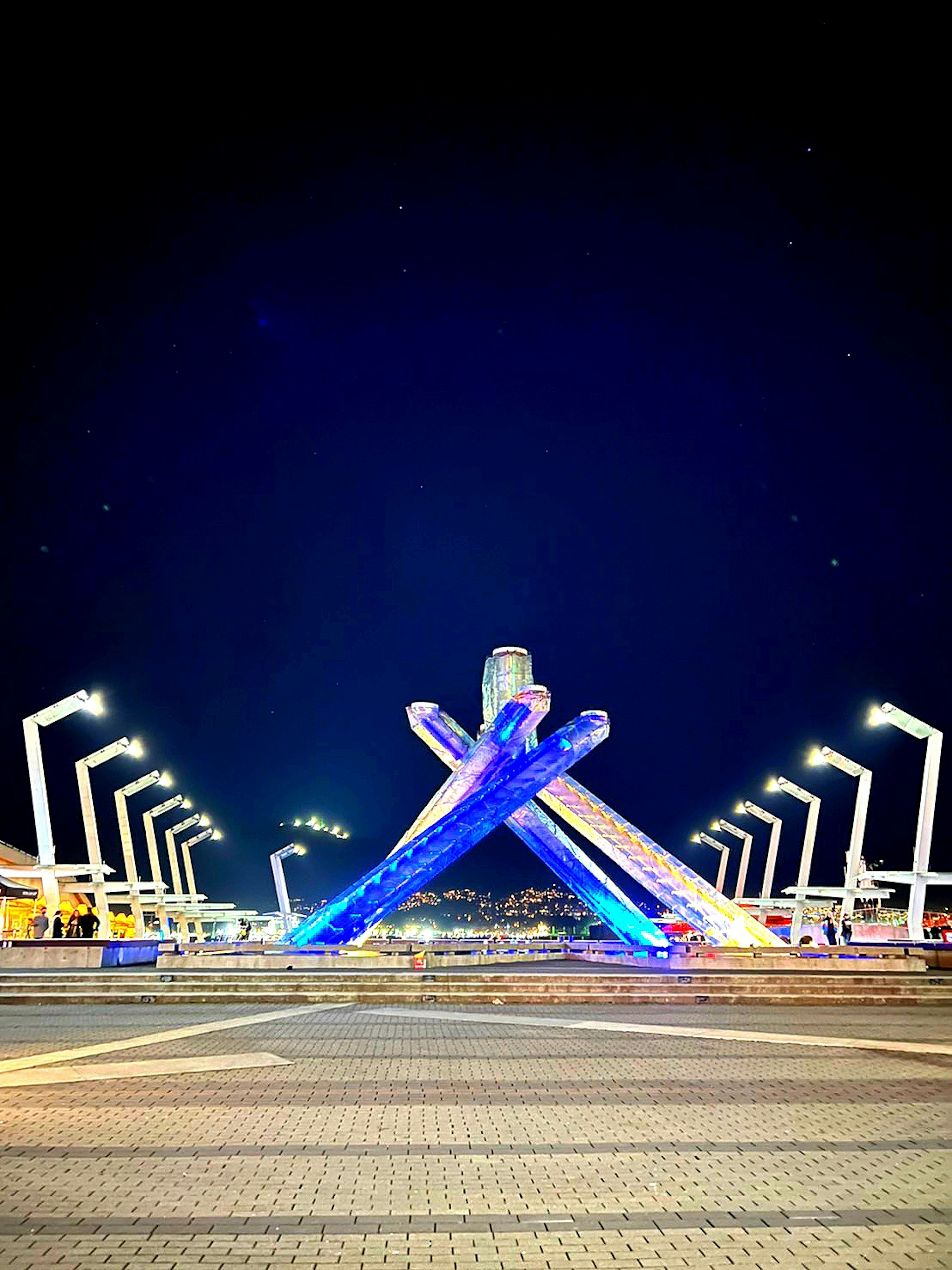 Night scene featuring a blue illuminated monument with intersecting structures and streetlights