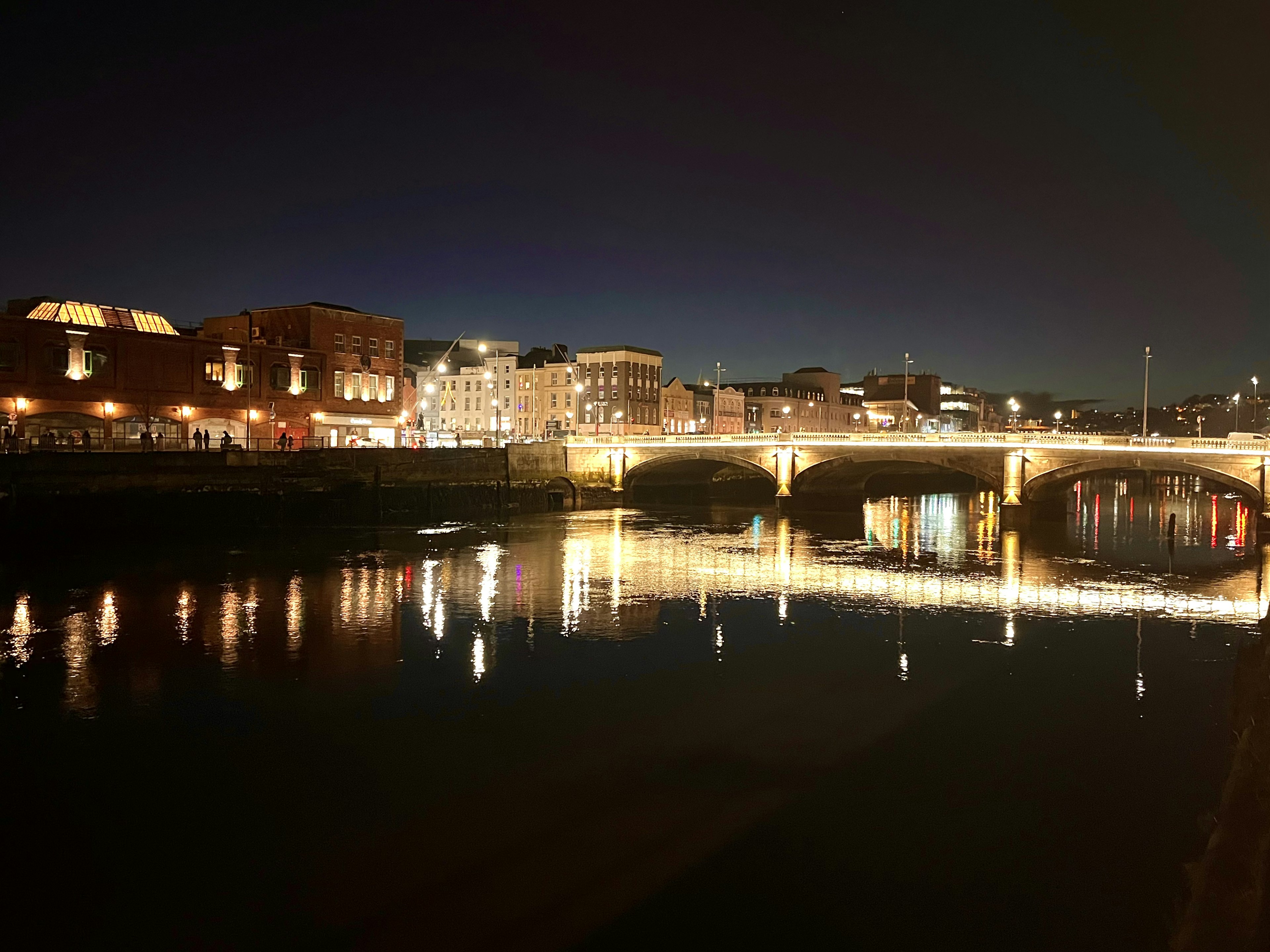 Nächtliche Aussicht auf einen Fluss und eine Brücke mit reflektierenden Stadtlichtern