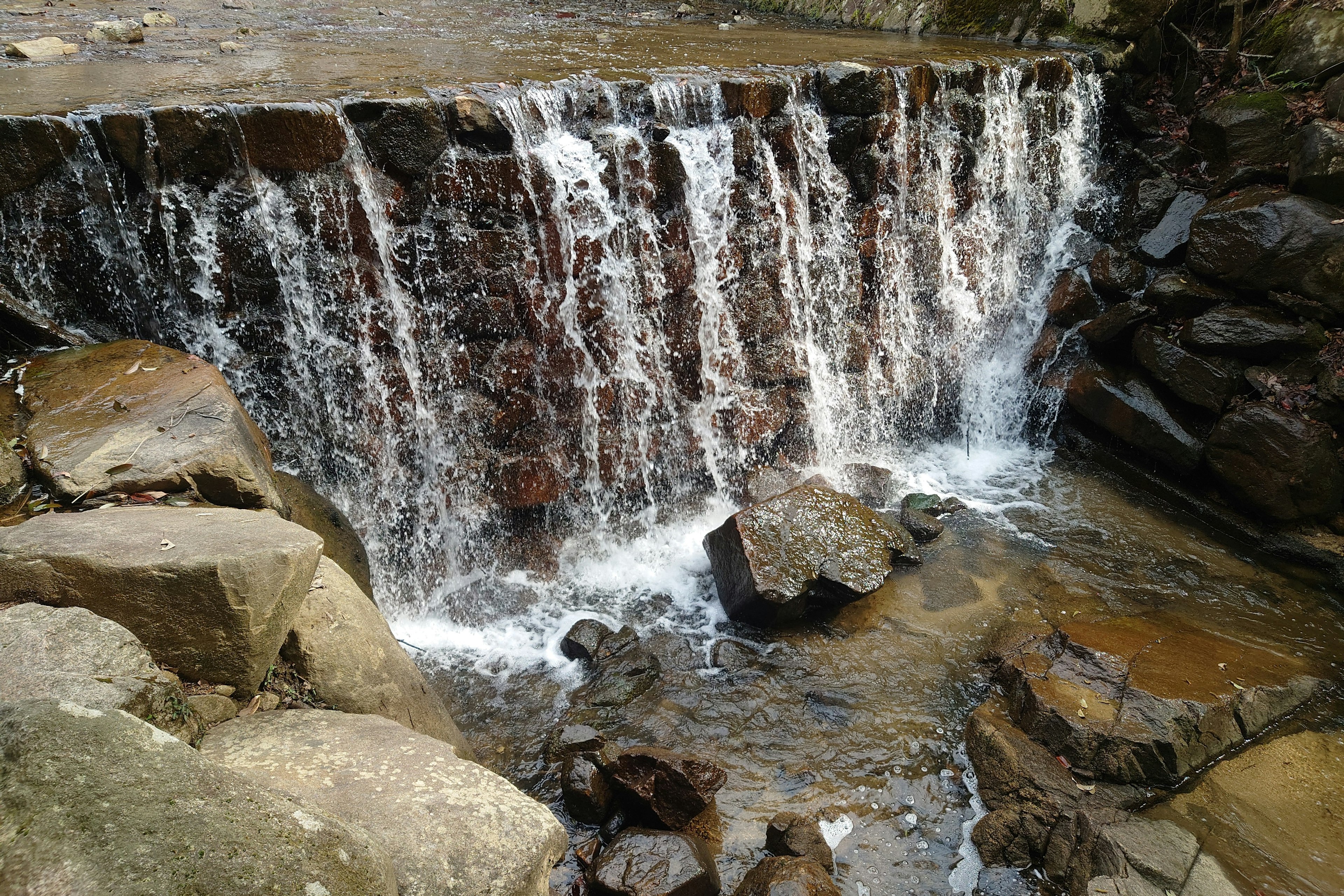 Air terjun kecil mengalir di atas batu di lingkungan alami