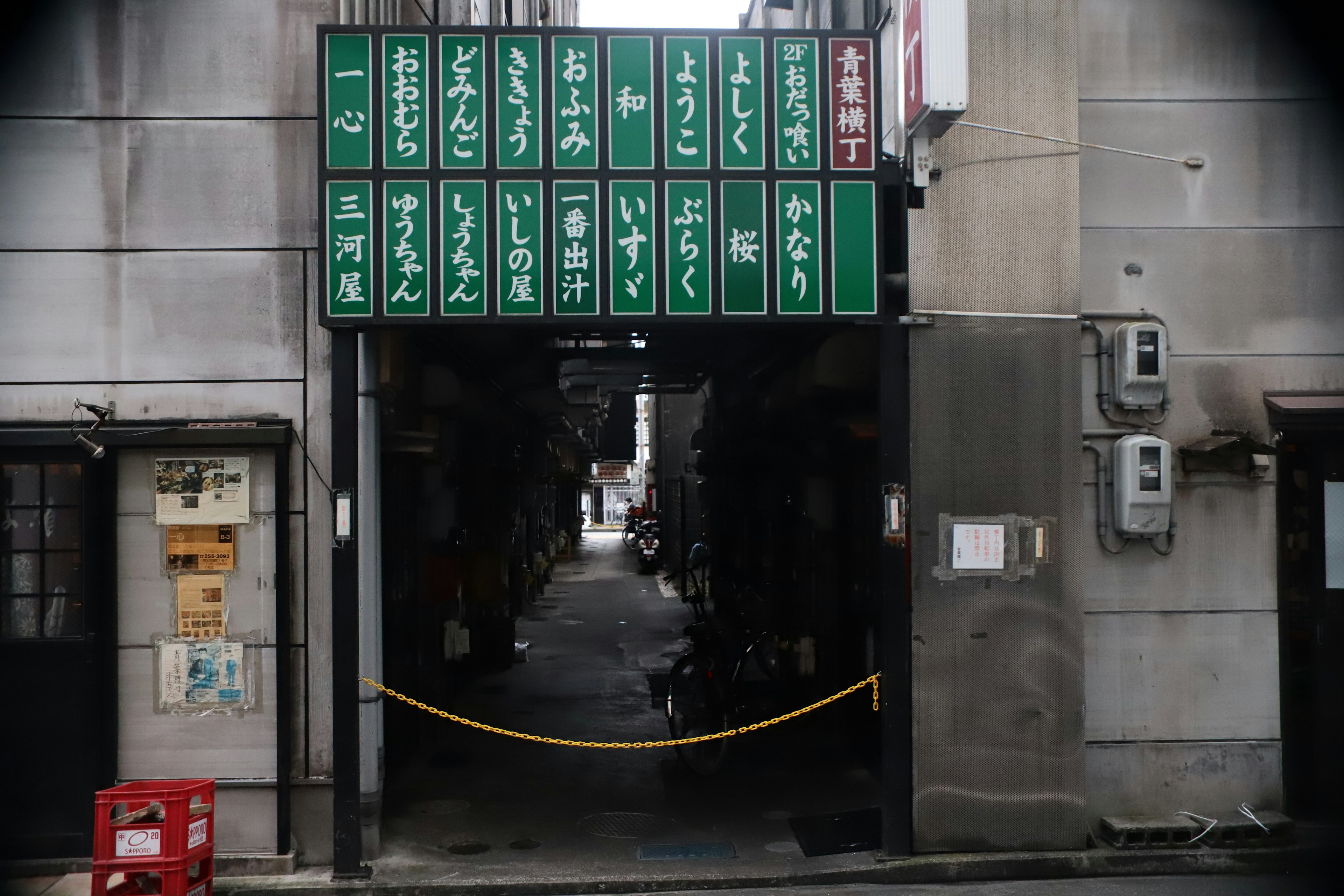 緑の看板が並ぶ狭い路地への入口の写真