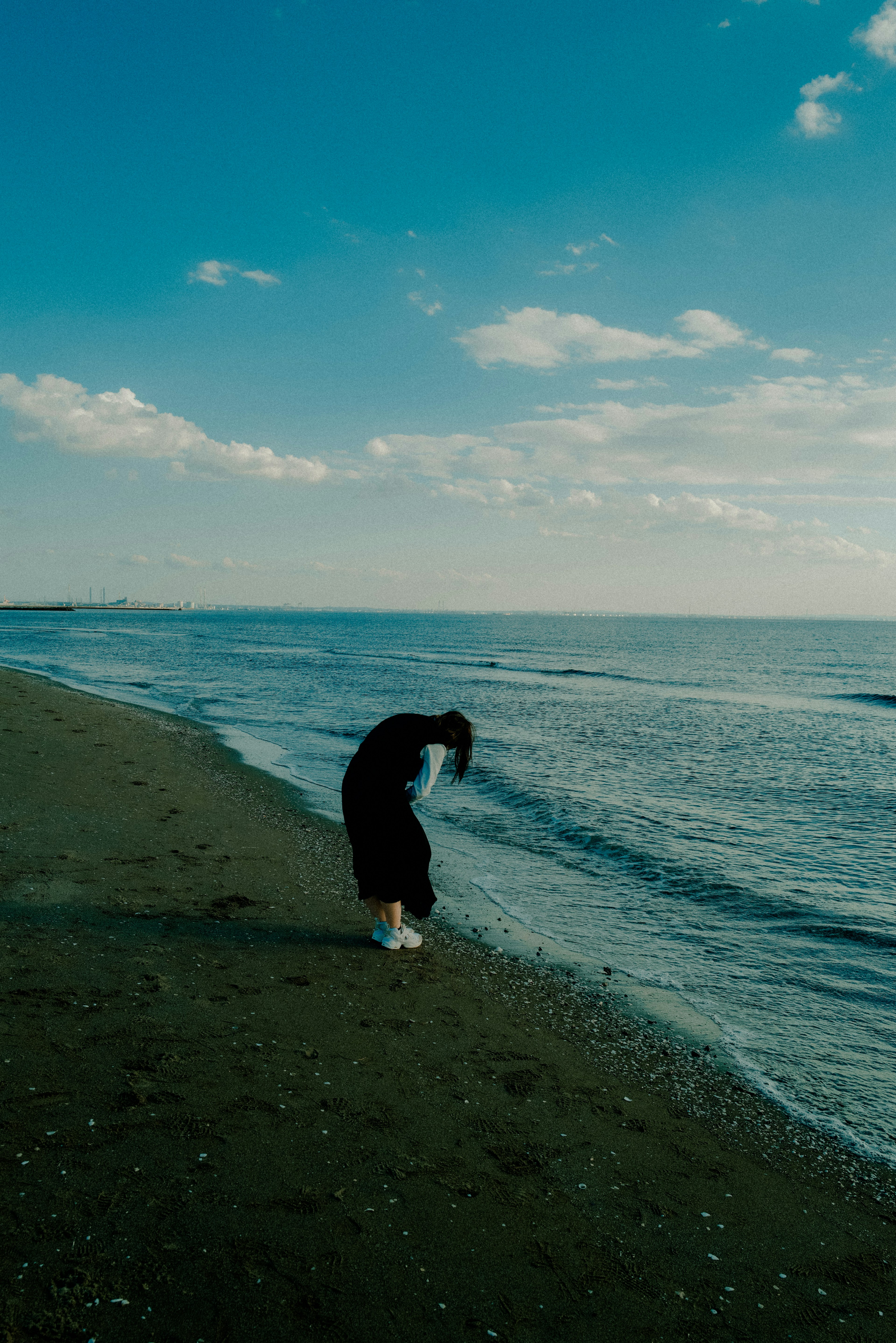 Persona haciendo un pino en la playa con cielo azul y nubes blancas