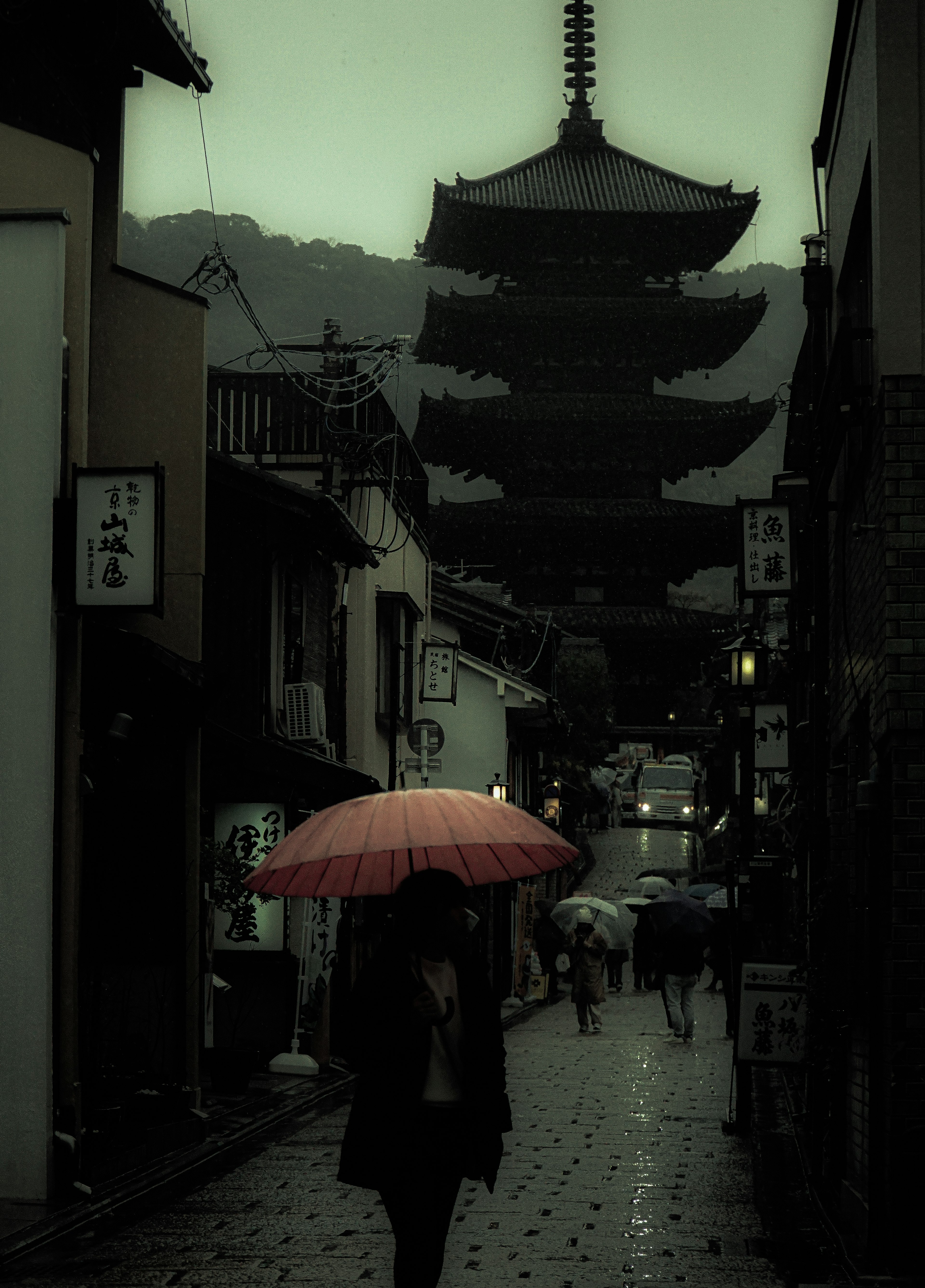 雨の中の赤い傘を持った人と古い塔のある街並み