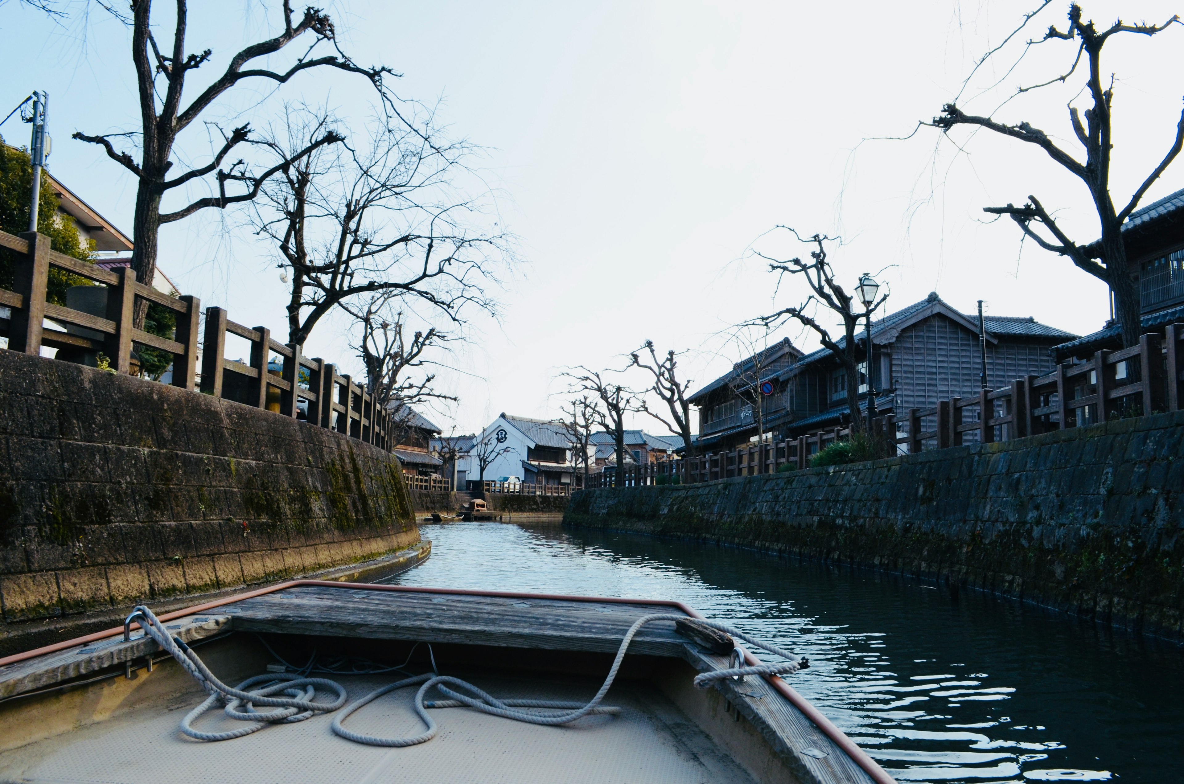 View from a small boat on a quiet canal featuring bare trees and traditional houses along the banks