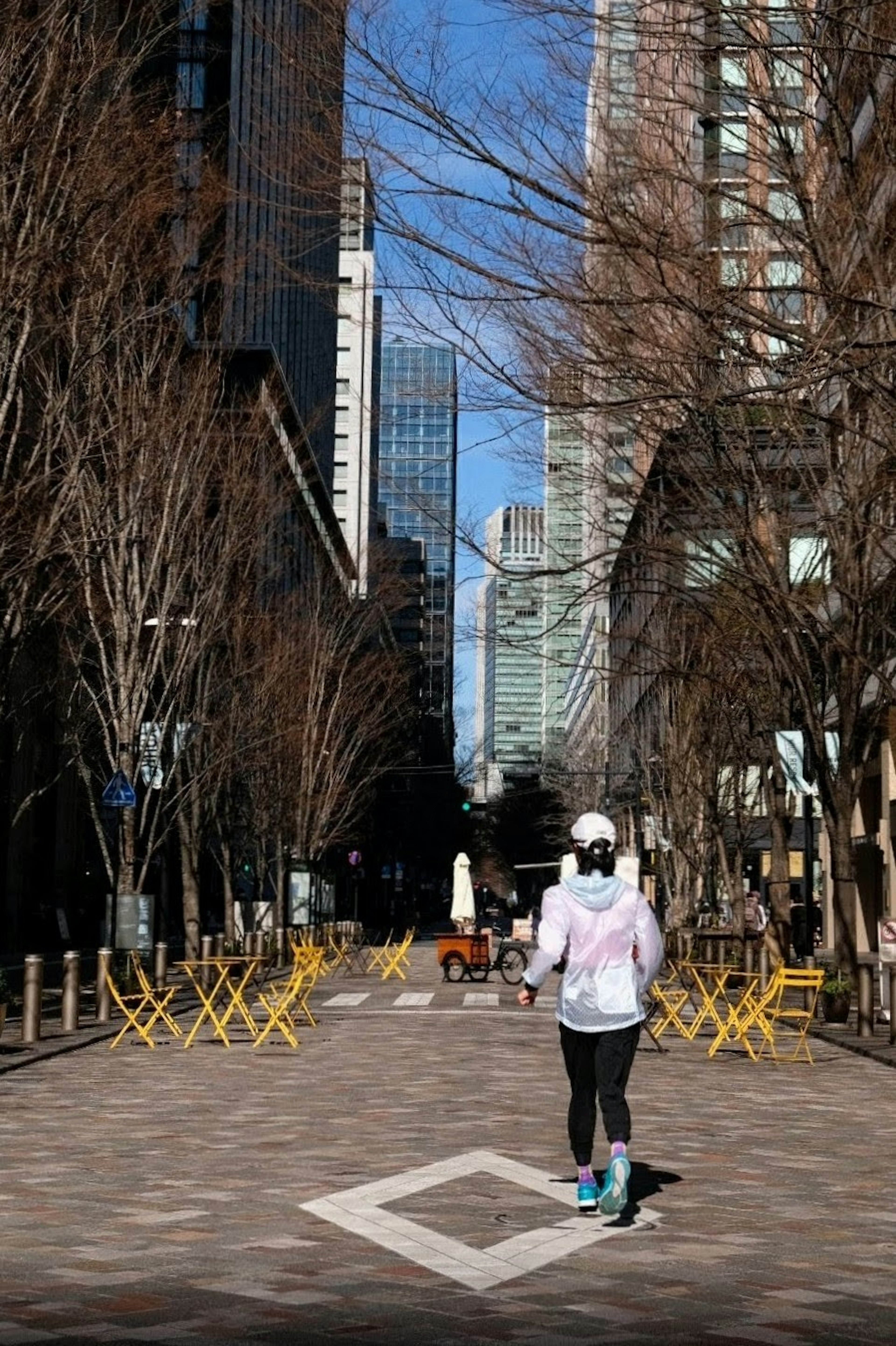 A person running on a street surrounded by tall buildings wearing a white jacket and hat