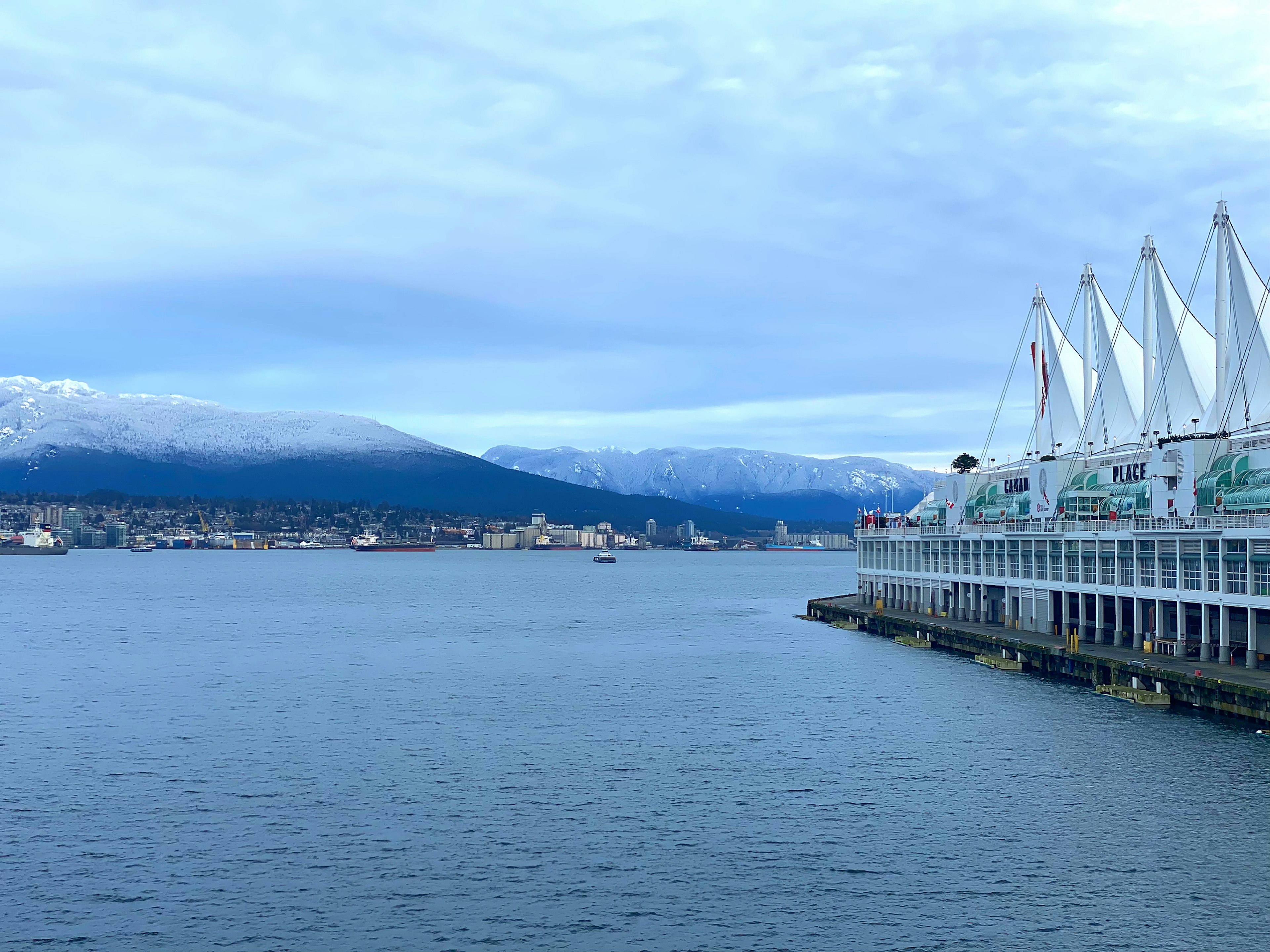 View of blue water with snowy mountains and white tent-like structures along the waterfront