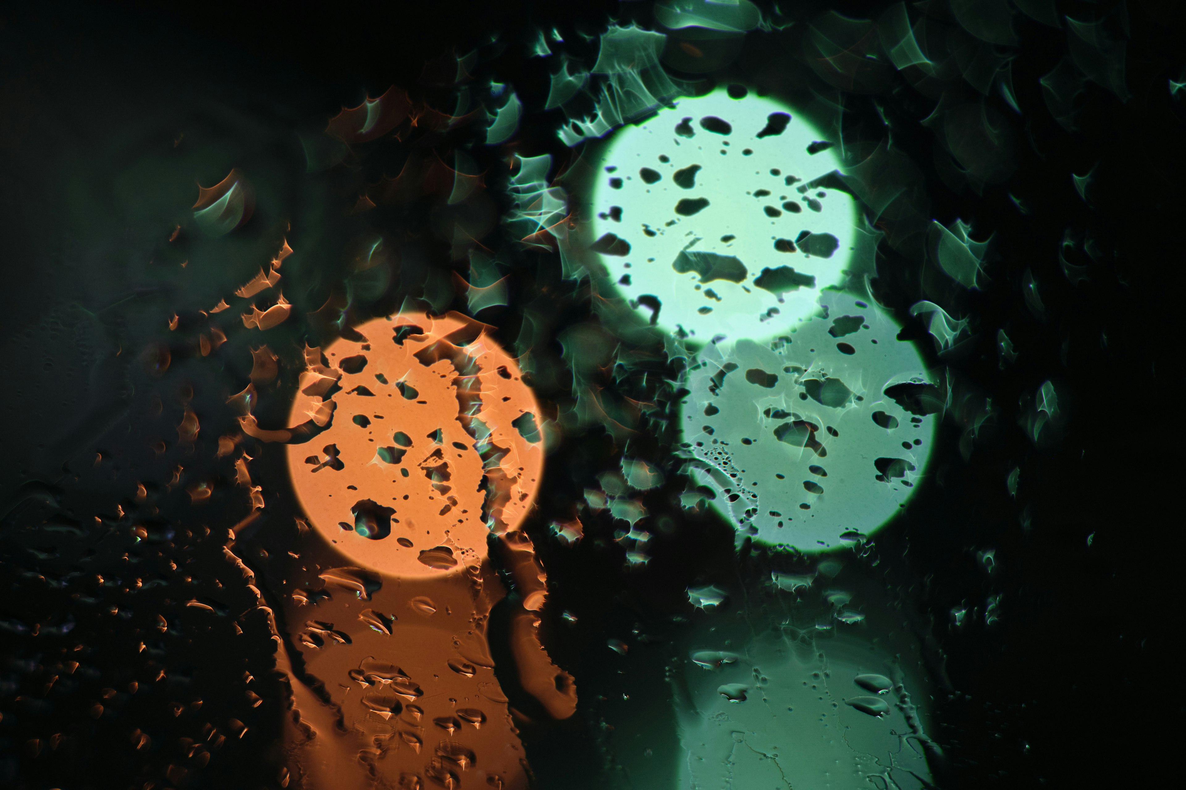 Orange and green lights seen through a raindrop-covered glass