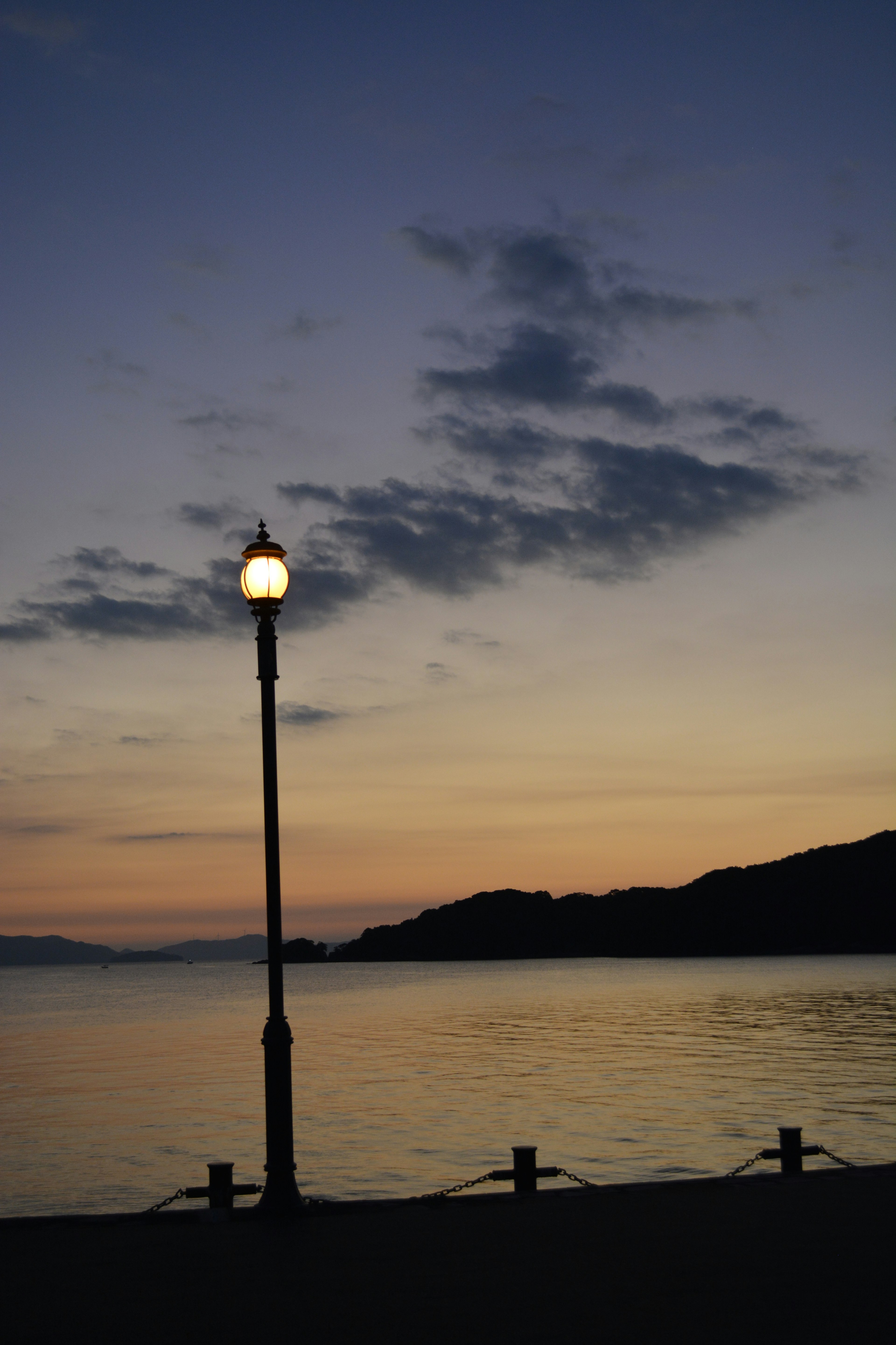 Street lamp silhouetted against a twilight sky and calm water