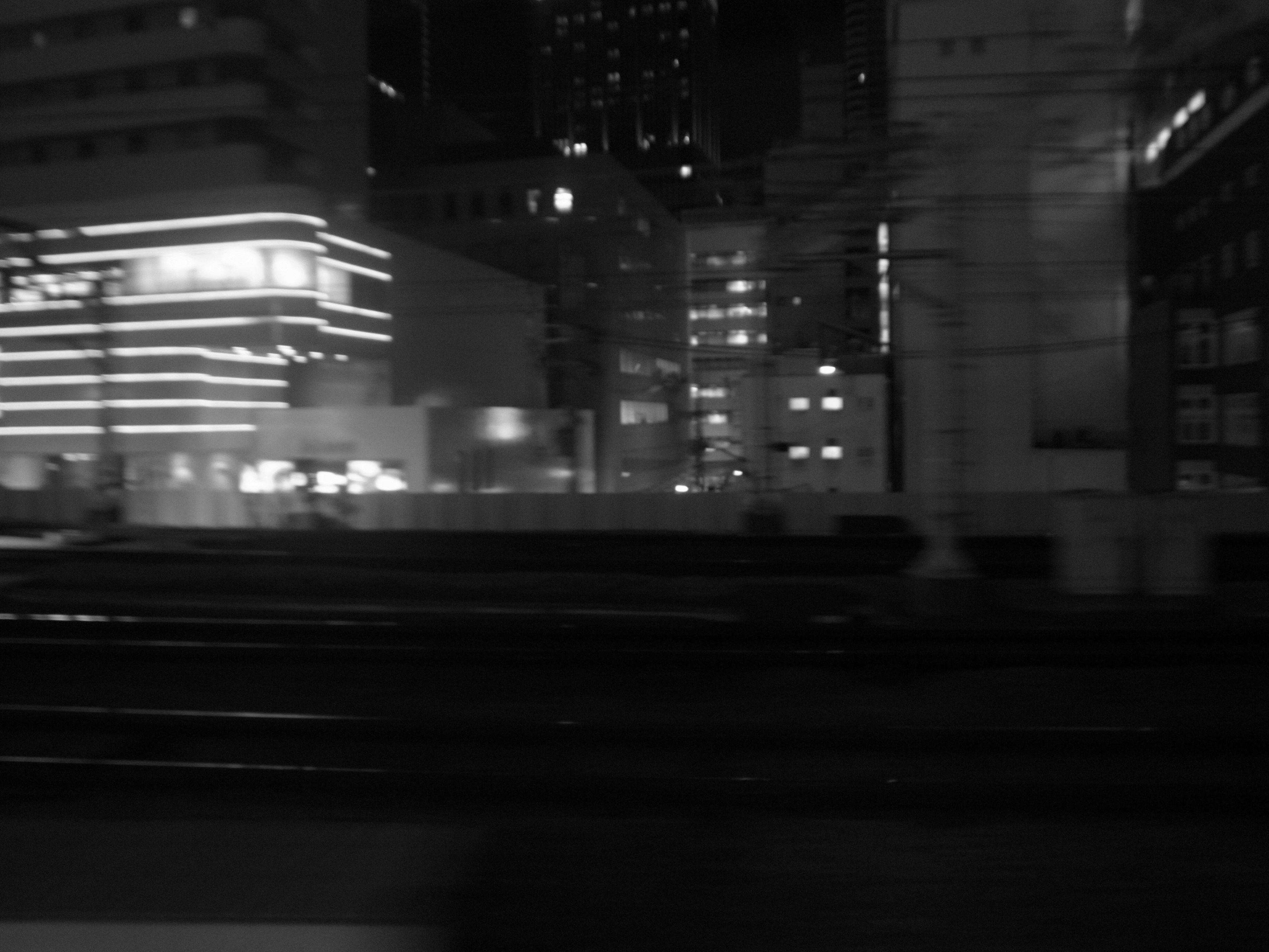 Nighttime cityscape with illuminated buildings and blurred train tracks