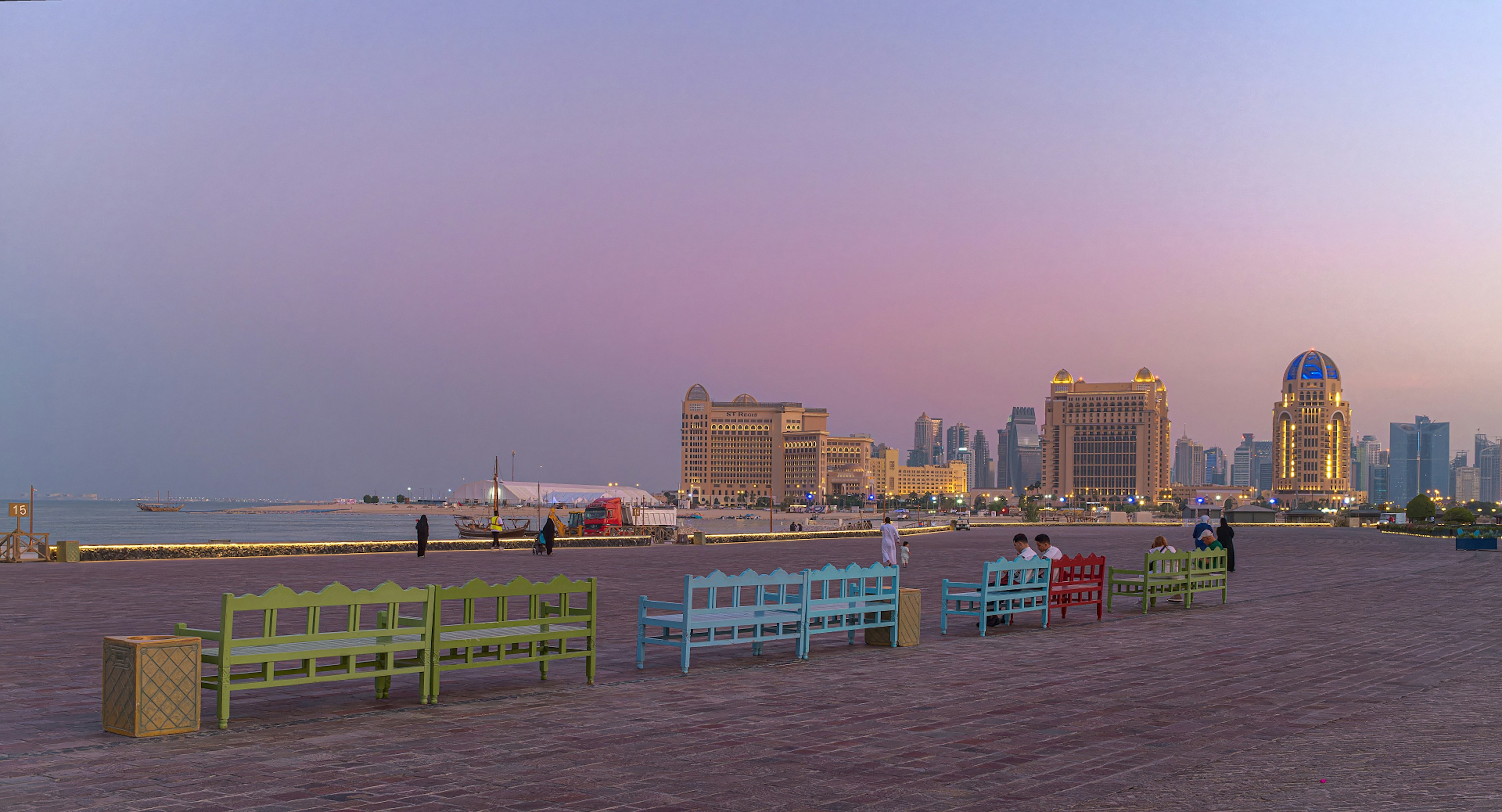 Colorful benches on a beach during sunset with a distant city skyline in Qatar