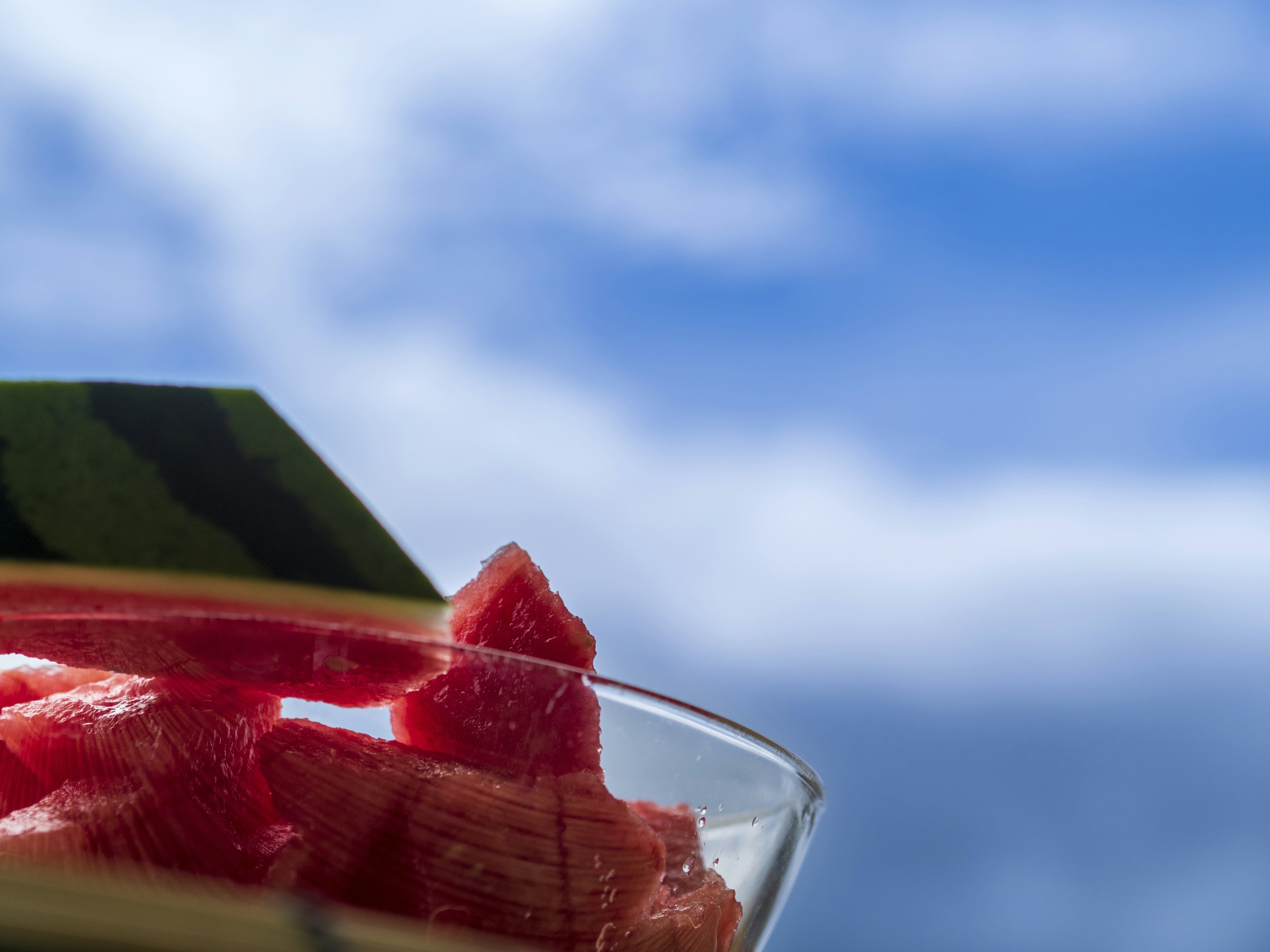 A clear bowl with watermelon slices against a blue sky