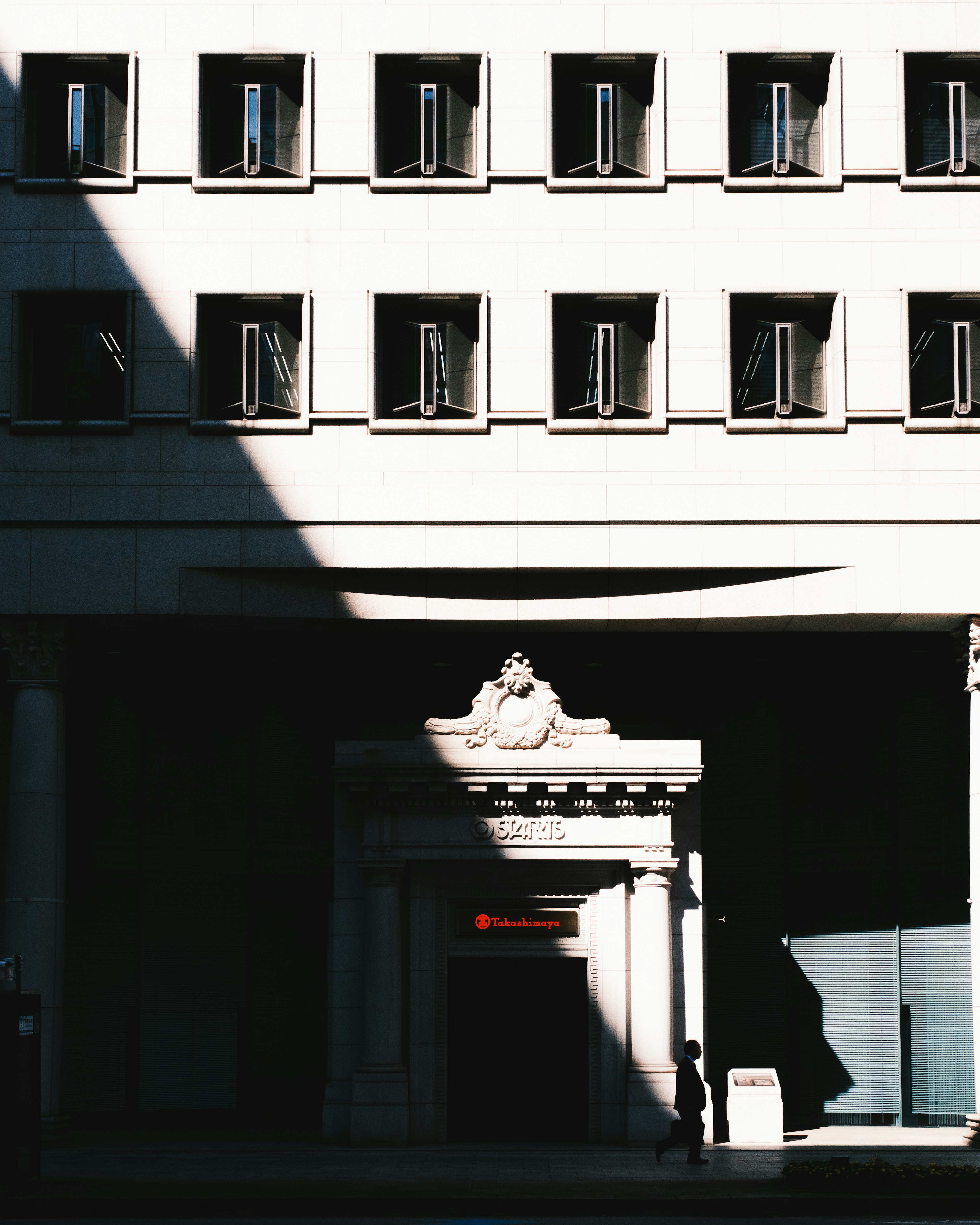 Fassade eines Gebäudes mit Schatten und einem dekorativen Eingang