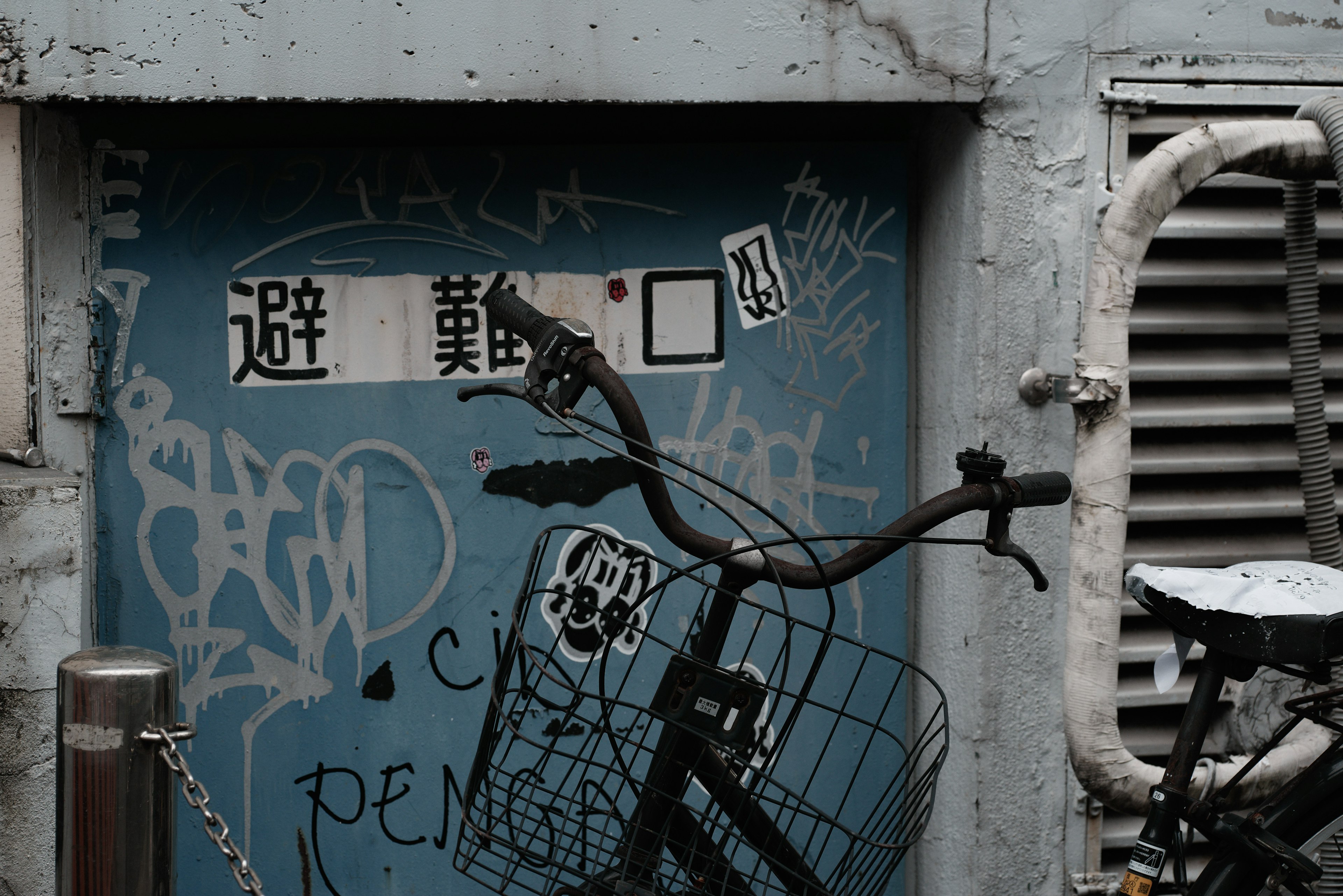 Bicycle with a wire basket in front of a blue wall covered in graffiti