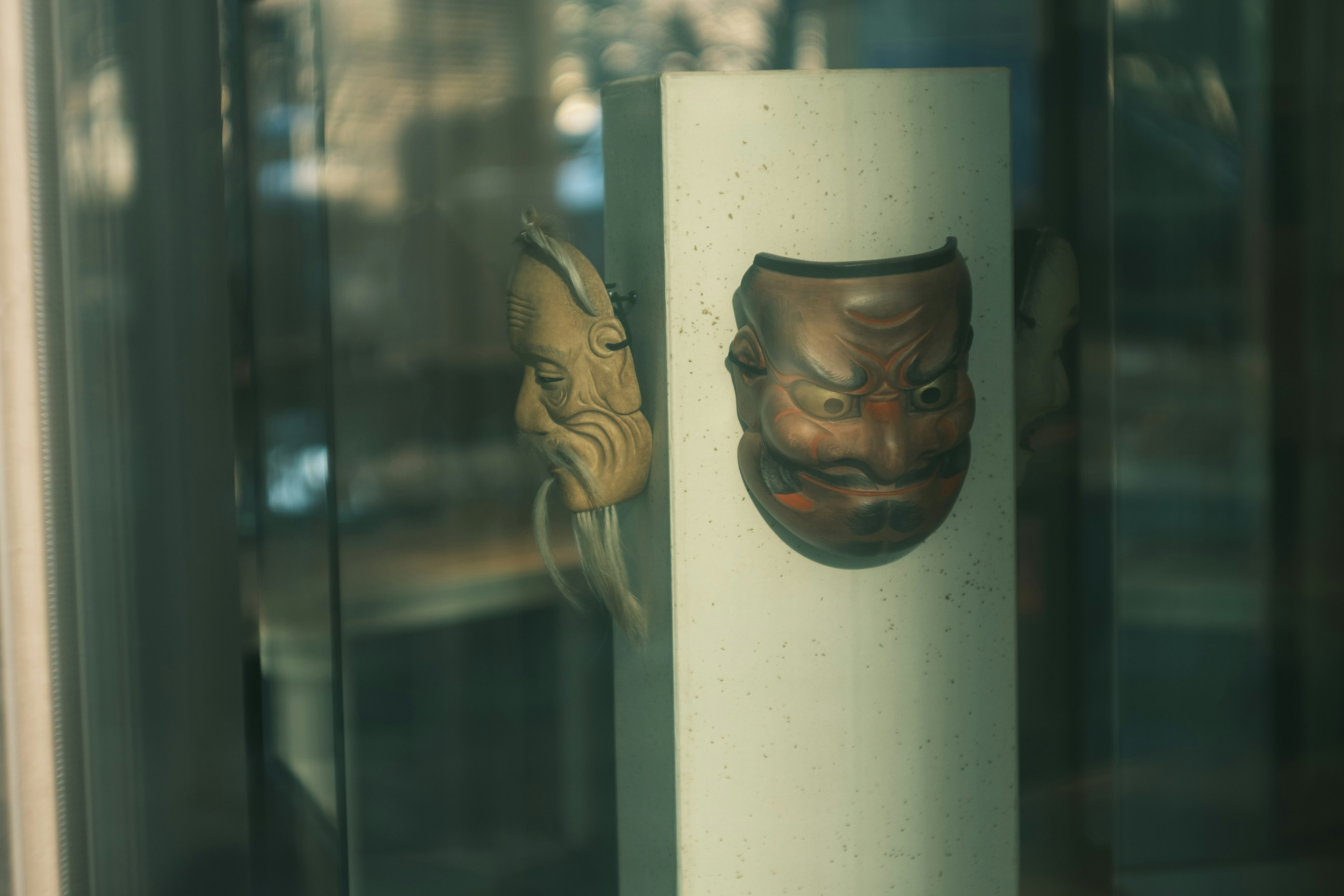 Two traditional Japanese masks displayed in a glass case