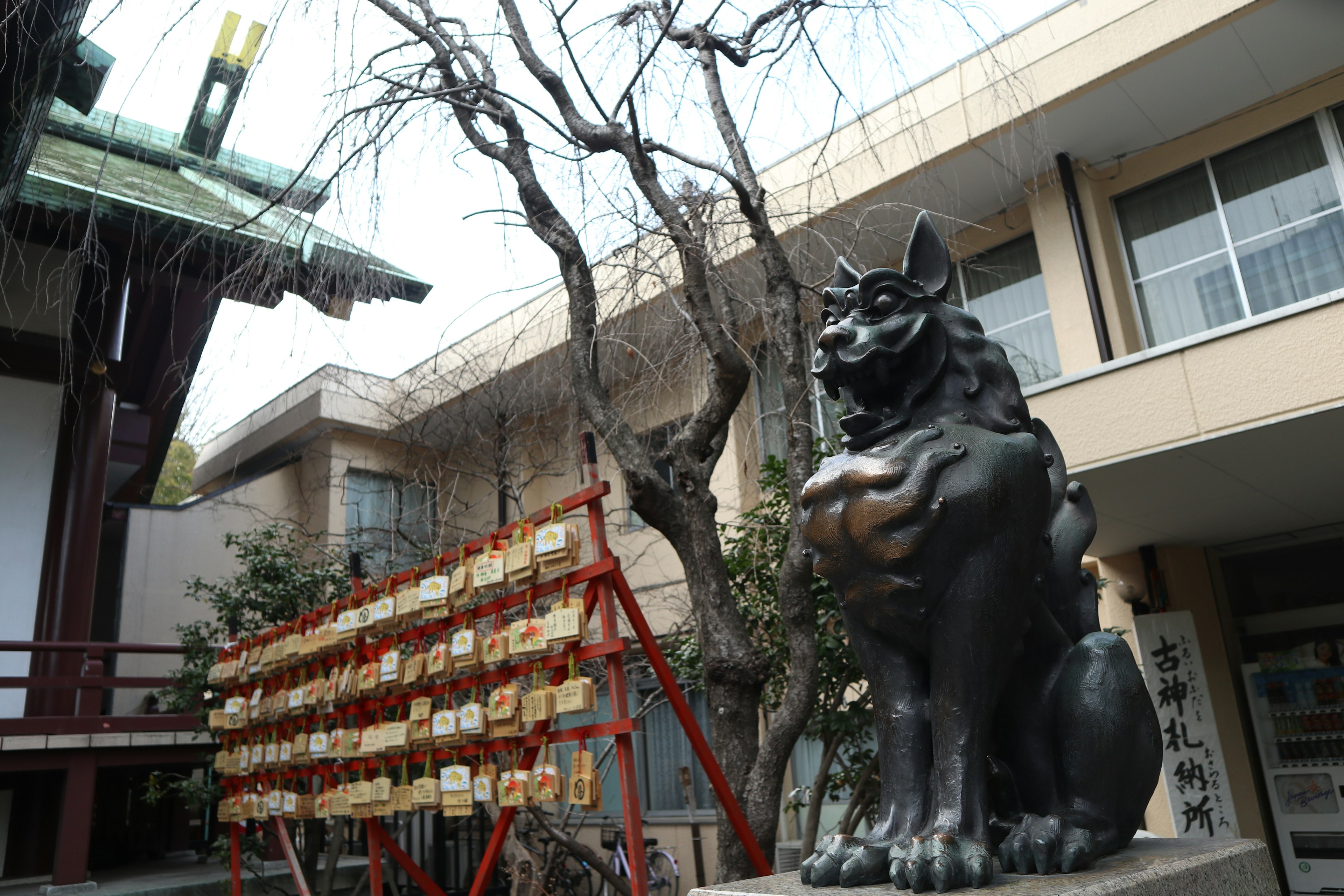 Estatua de komainu negro frente a un santuario con árboles