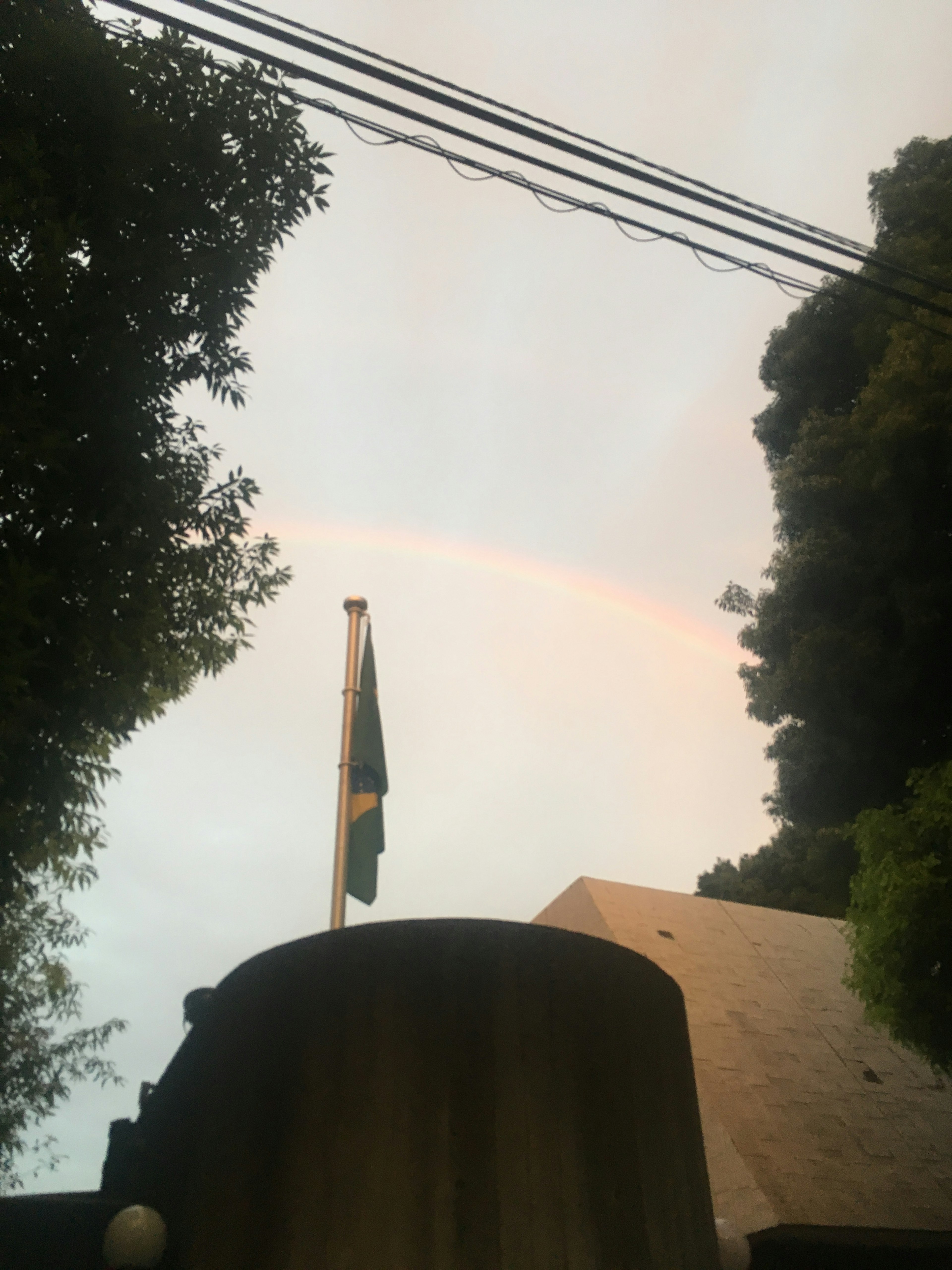 A rainbow arching across the sky with a visible Brazilian flag