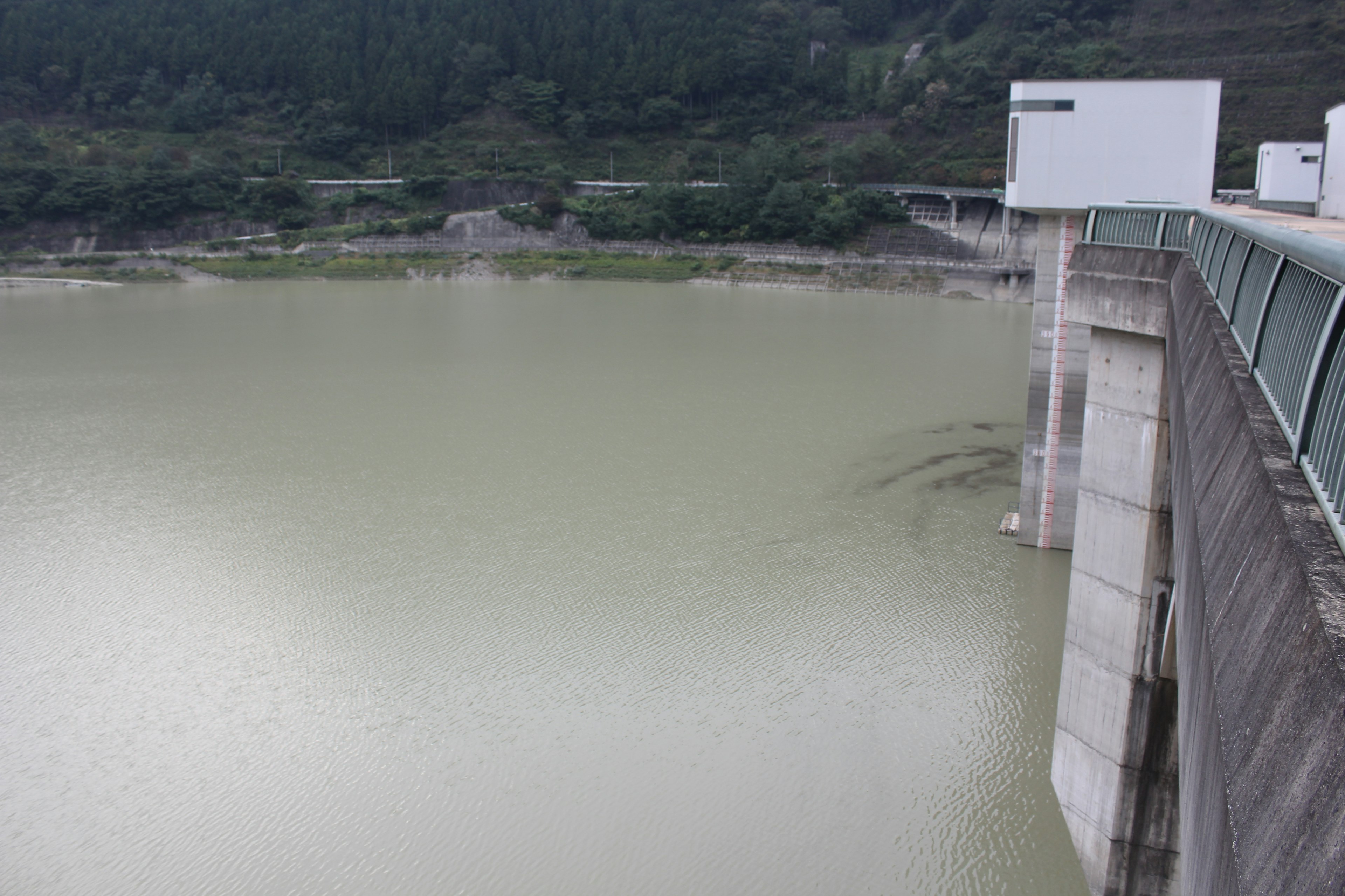 Betonstruktur eines Damms mit trübem grünem Wasserspiegel