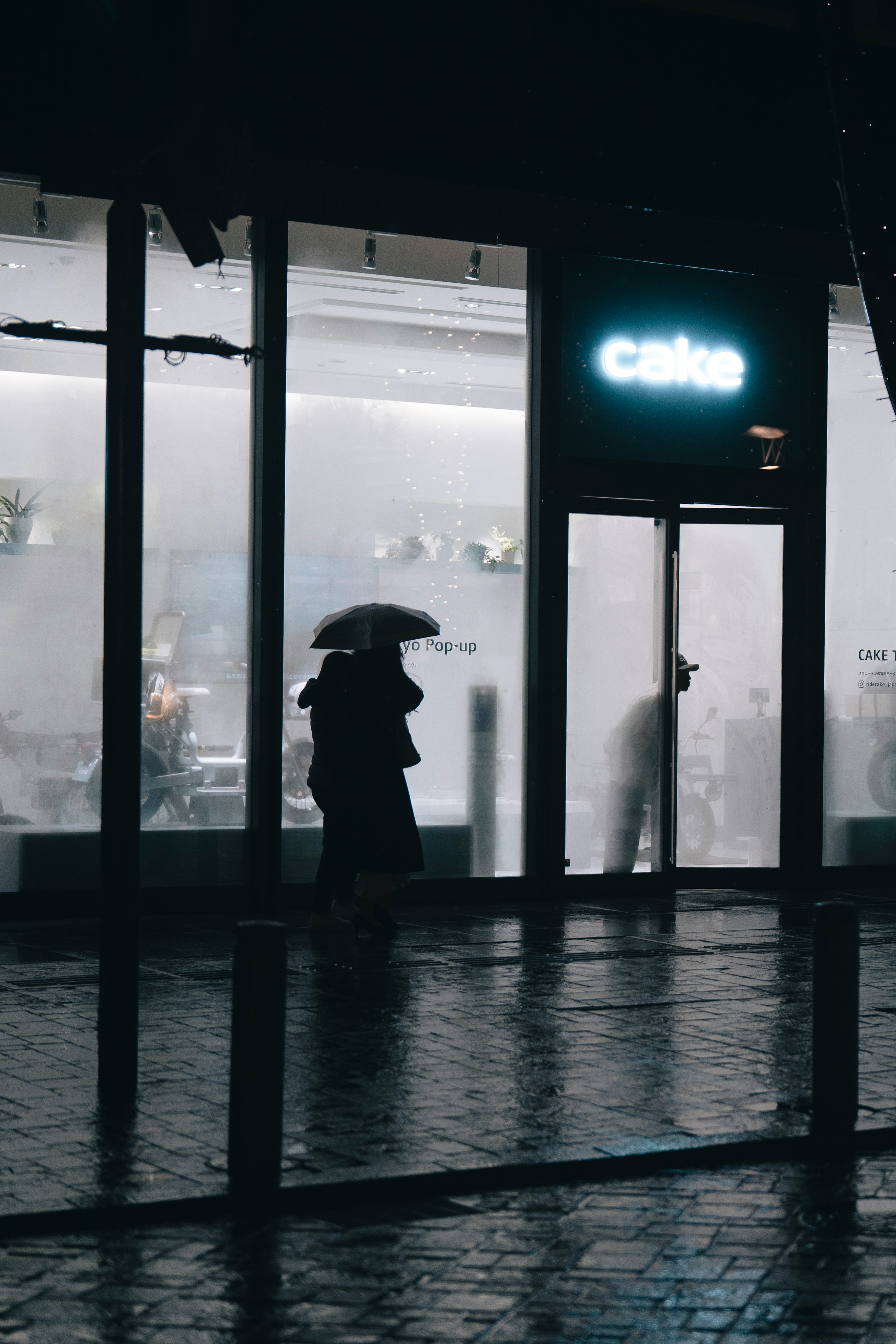 在雨夜中，拿着伞的剪影在咖啡馆前