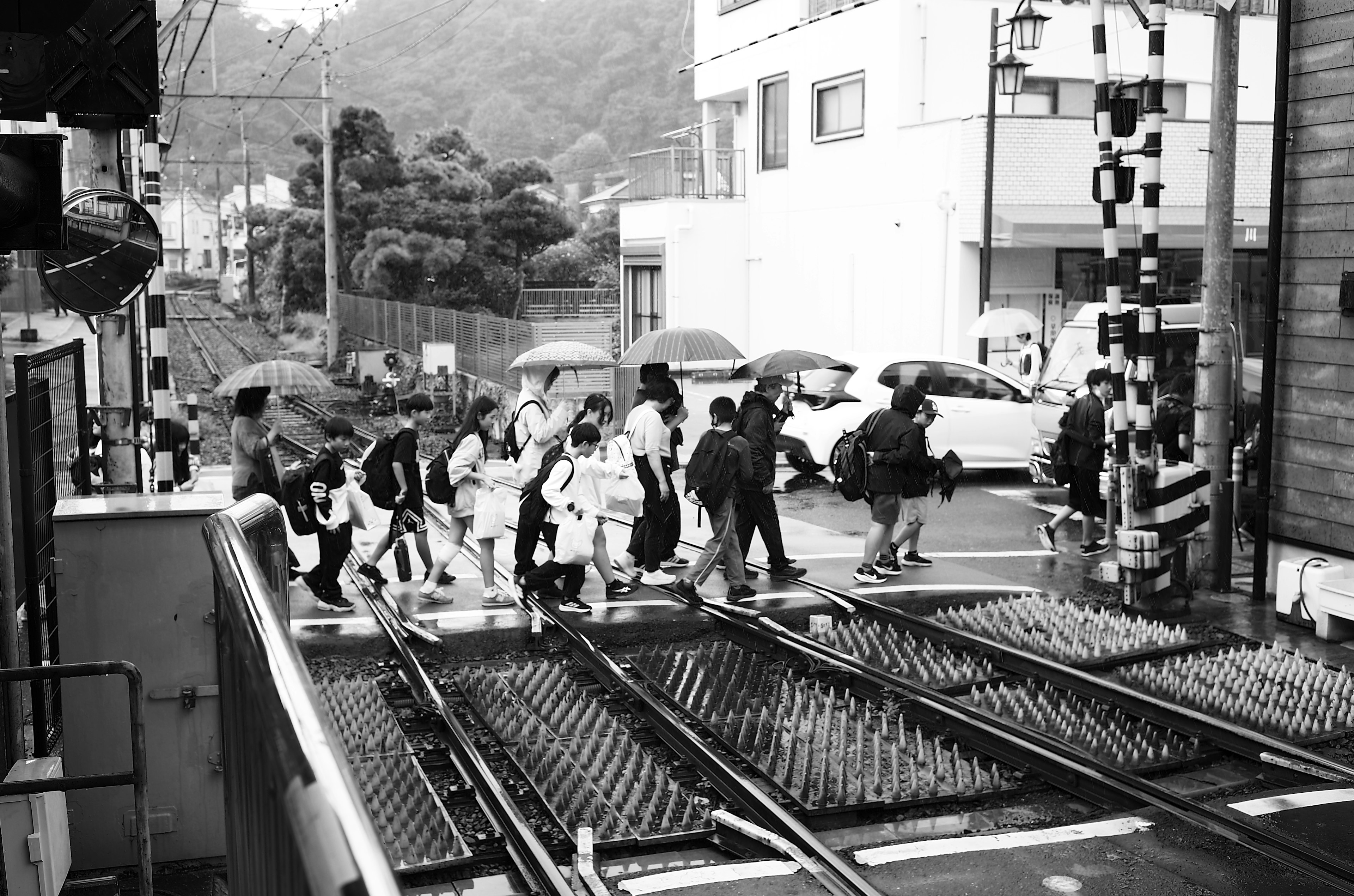 Foto en blanco y negro de personas cruzando un paso a nivel con paraguas bajo la lluvia