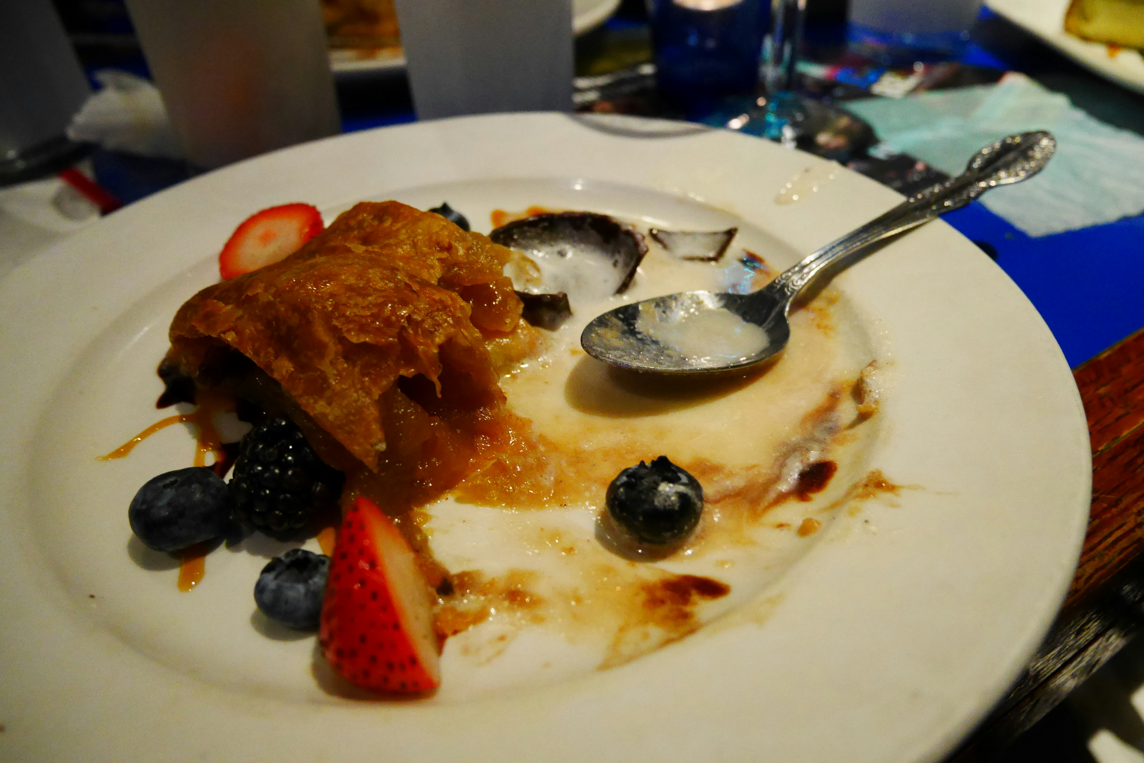 Dessert plate with remnants of berries and cream alongside a piece of apple pie