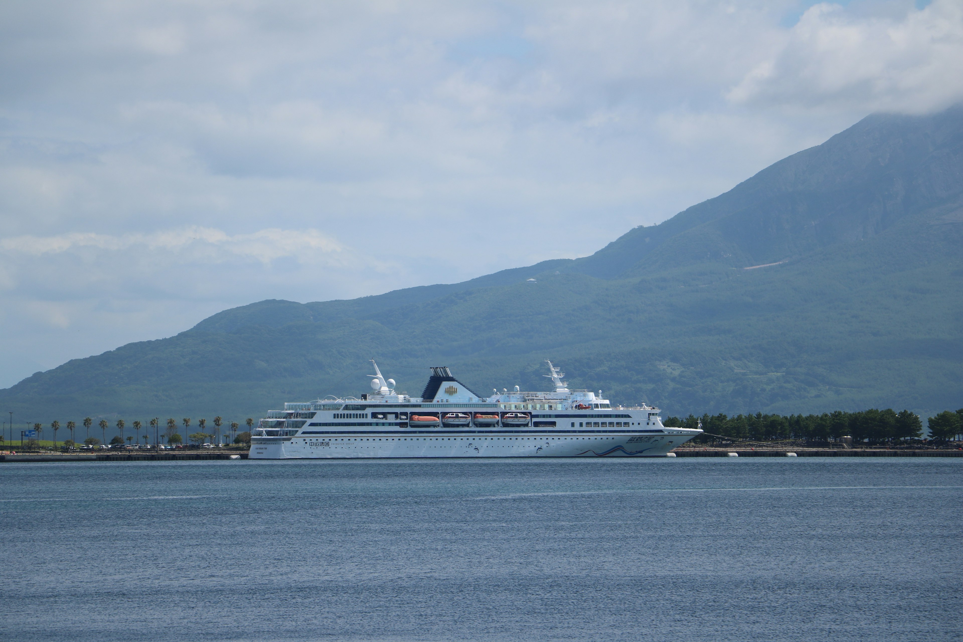 Cruise ship docked against a backdrop of blue sea and mountains