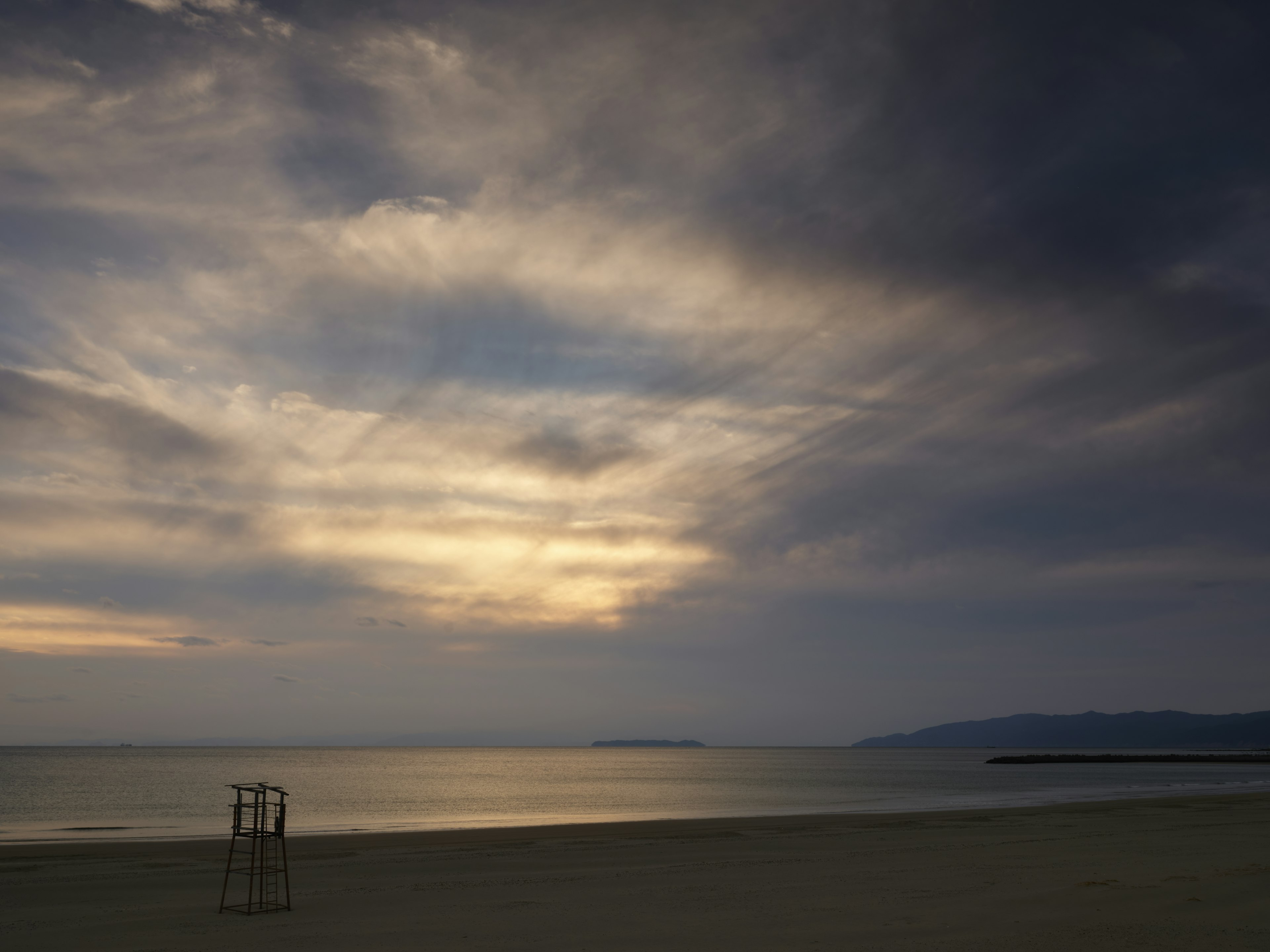 Costa tranquila con nubes oscuras rodeando un atardecer sobre el mar