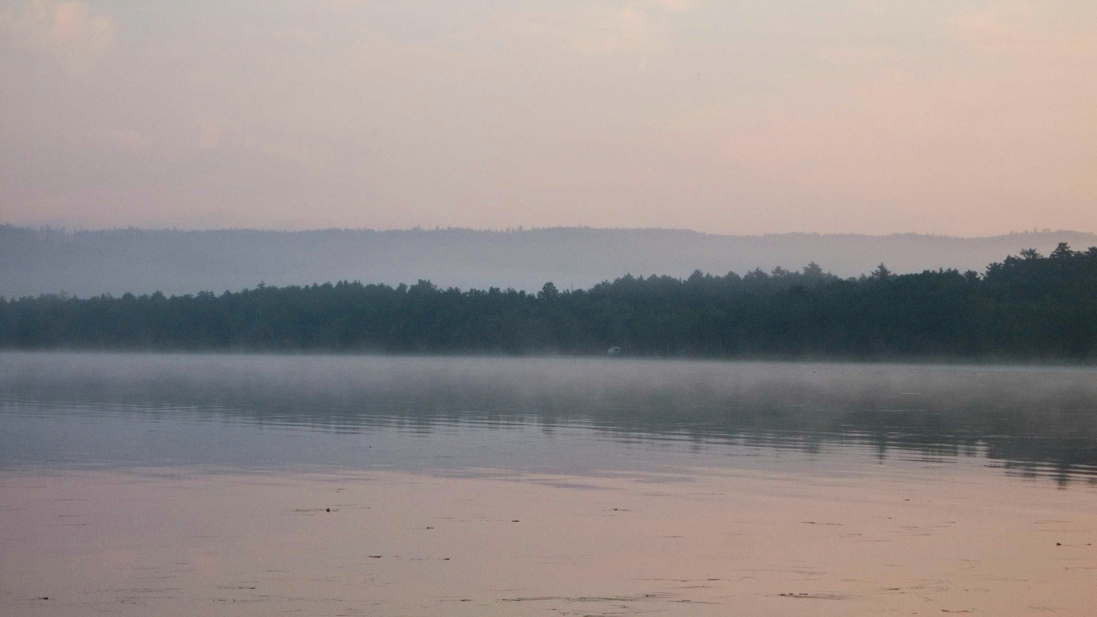 Danau tenang yang memantulkan nuansa lembut langit dan pegunungan