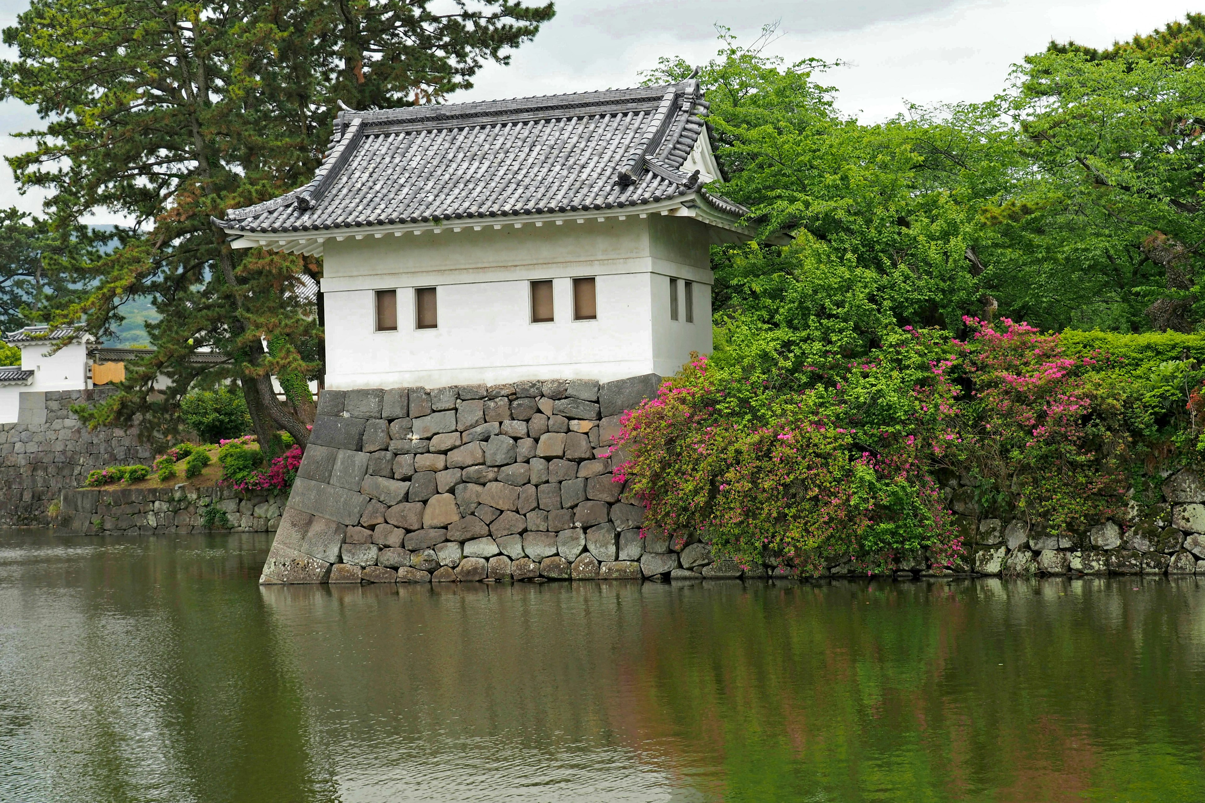 Edificio japonés tradicional junto a un estanque rodeado de muros de piedra blanca y árboles verdes