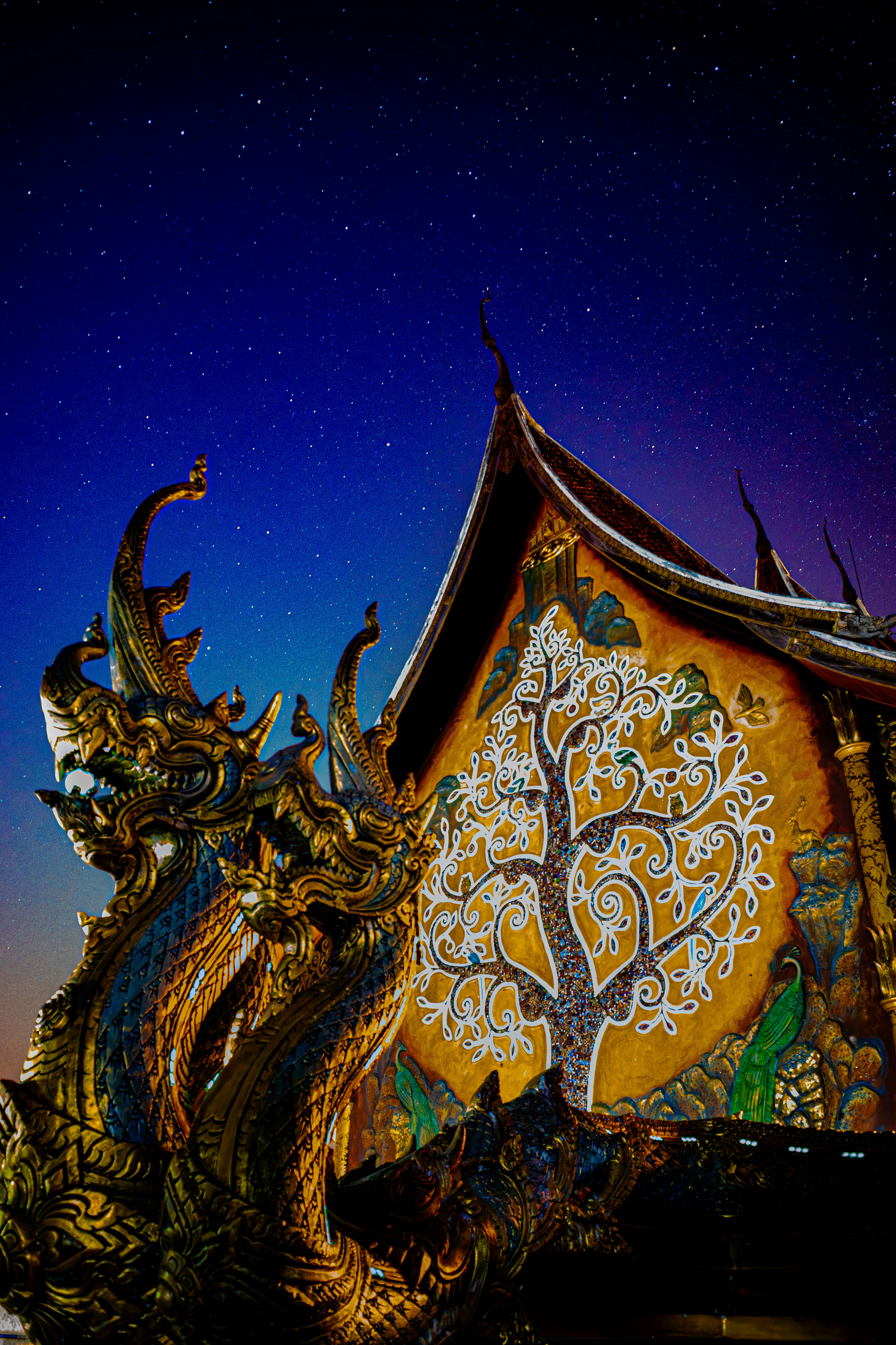 Temple wall featuring a tree design and dragon sculptures under a starry night sky