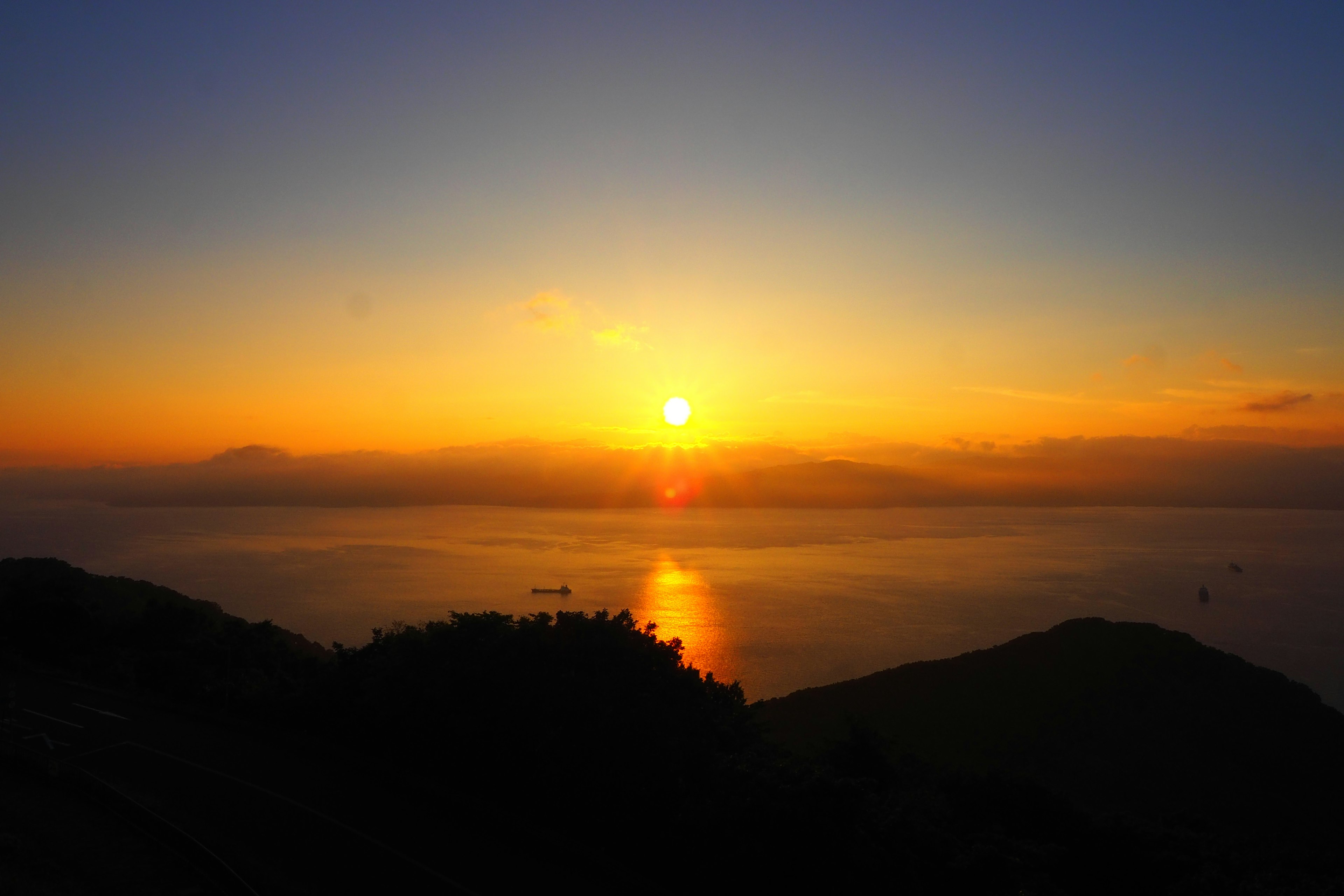 Pemandangan matahari terbenam yang menakjubkan di atas lautan dengan bukit bersiluet