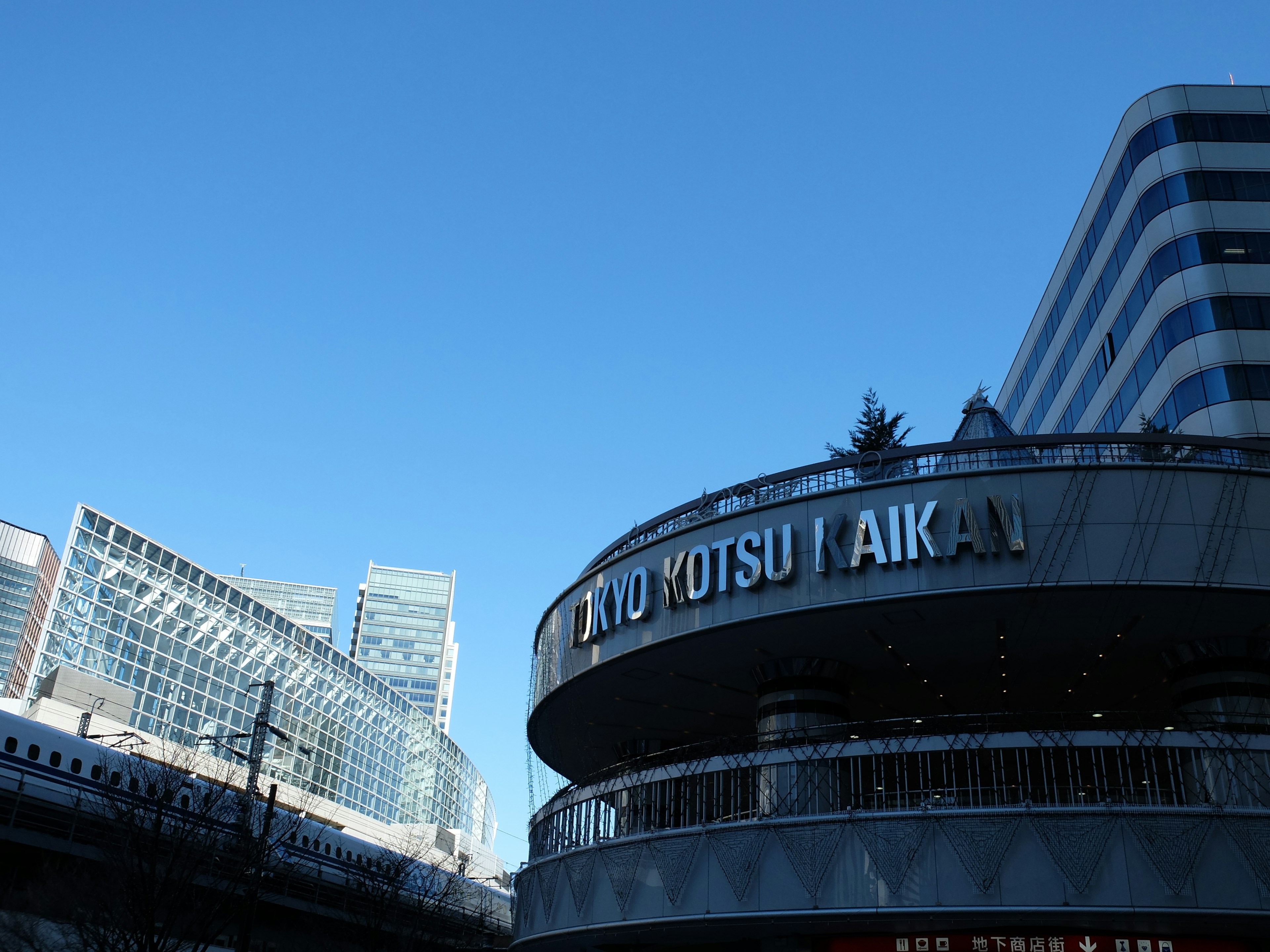 อาคารที่มีป้าย 'TO KOTSU AIKAI' ใต้ท้องฟ้าสีฟ้าใสพร้อมตึกระฟ้าสมัยใหม่