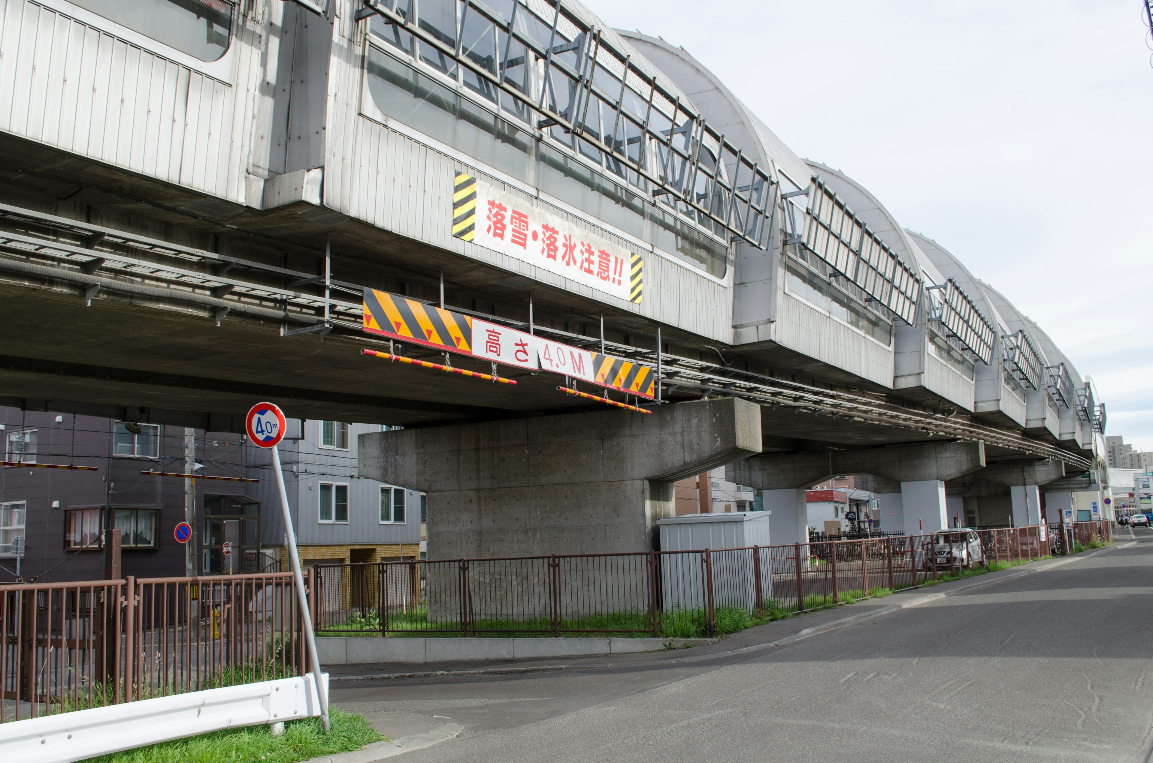 Vista di una strada sotto una ferrovia elevata con colonne di supporto e segnali di avvertimento