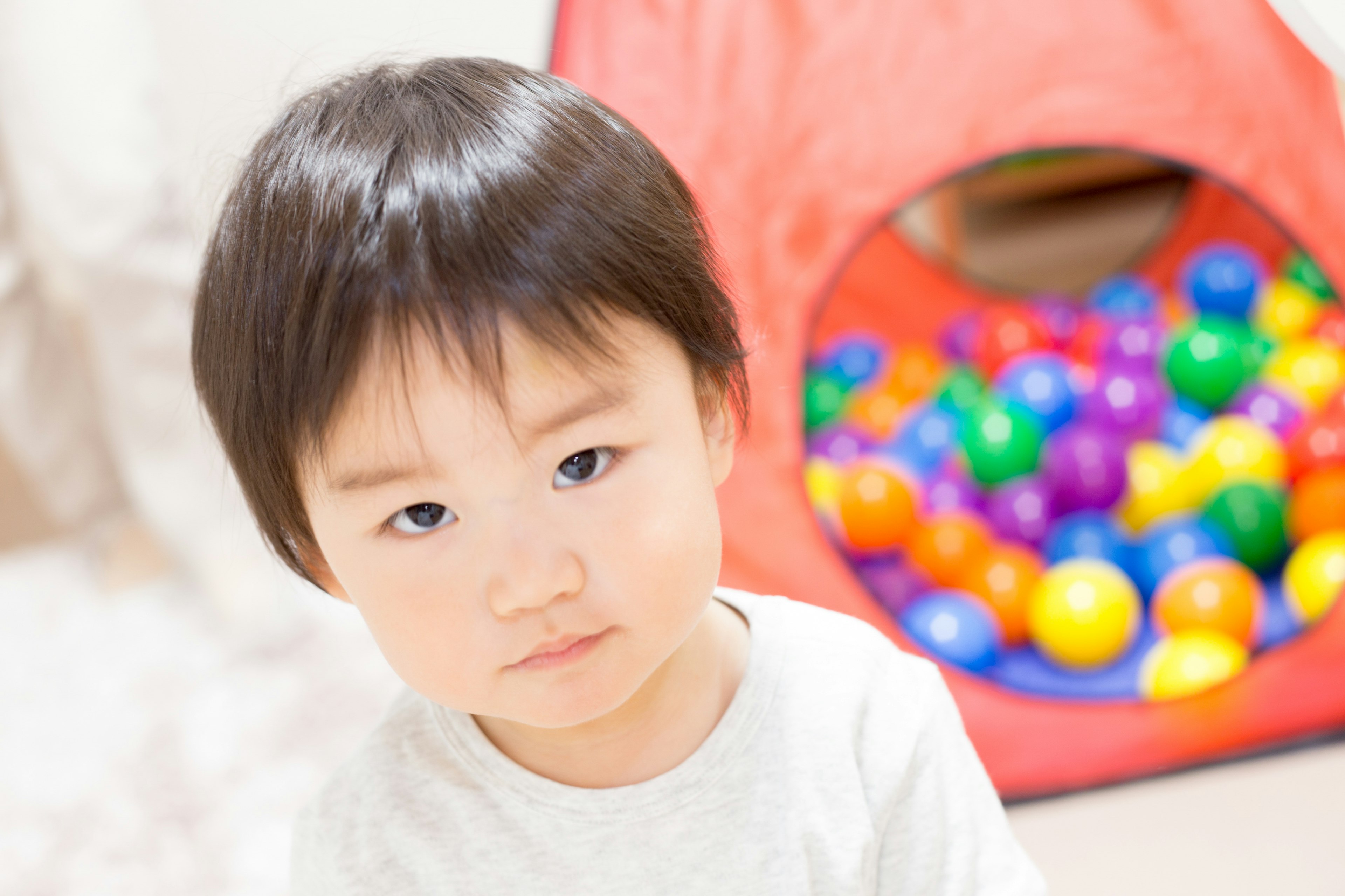 Ritratto di un bambino con espressione seria di fronte a una vasca di palline colorate