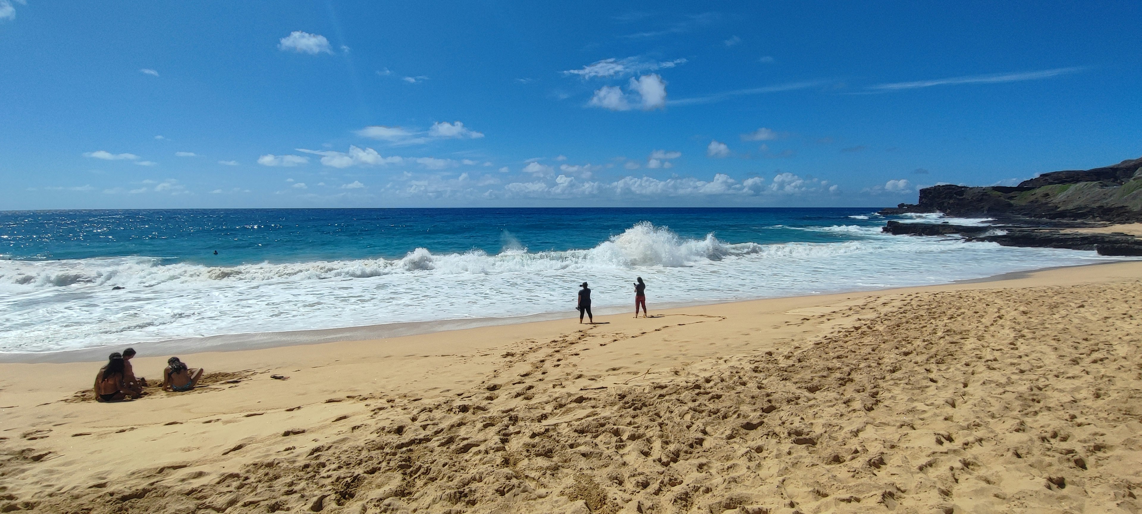 Zwei Personen, die an einem Strand mit blauem Ozean und weißen Wellen spazieren