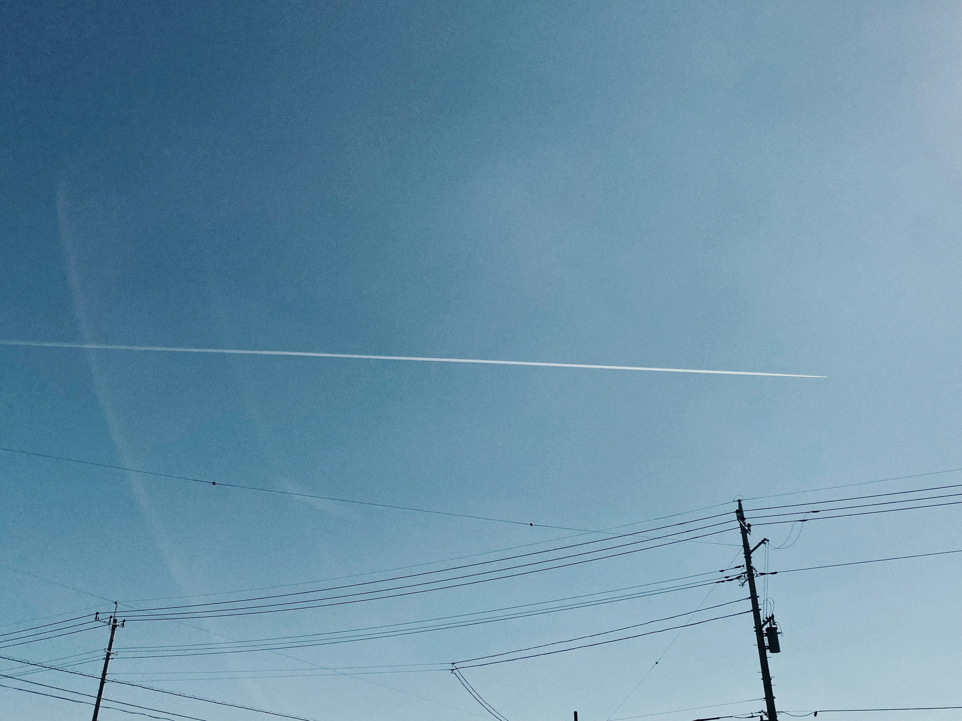 青空に飛行機雲が伸びる風景 電線が見える