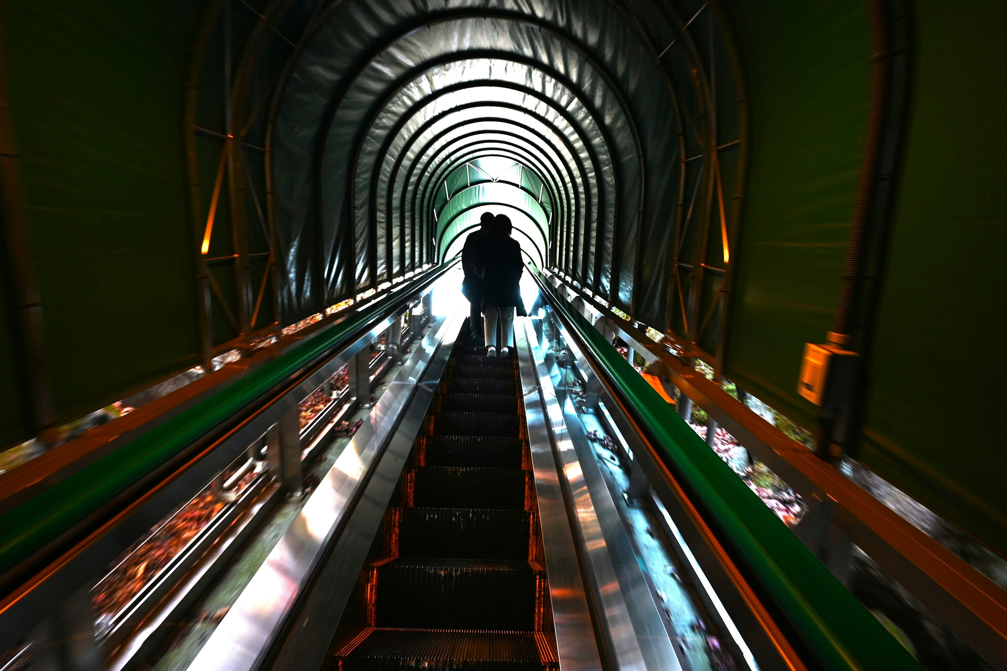 Foto de una escalera mecánica dentro de un túnel verde con siluetas de personas