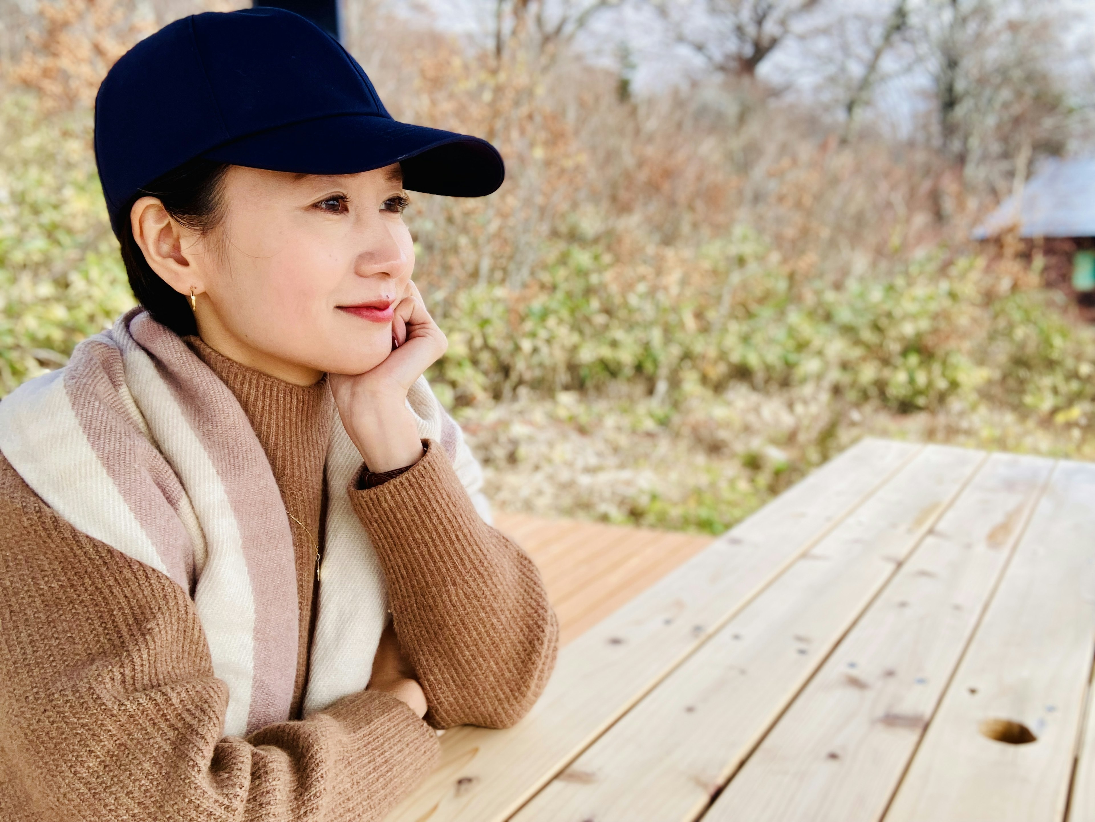 A woman wearing a casual cap resting her chin on her hand at a wooden table