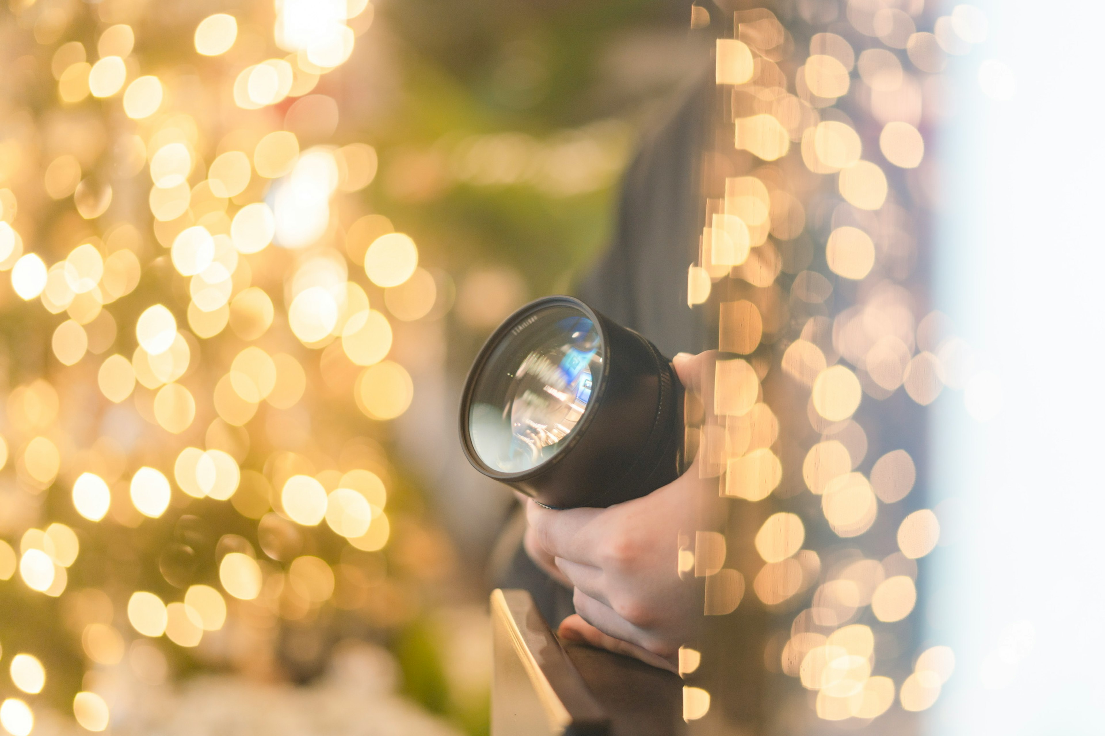 Camera lens held in hand with blurred background lights