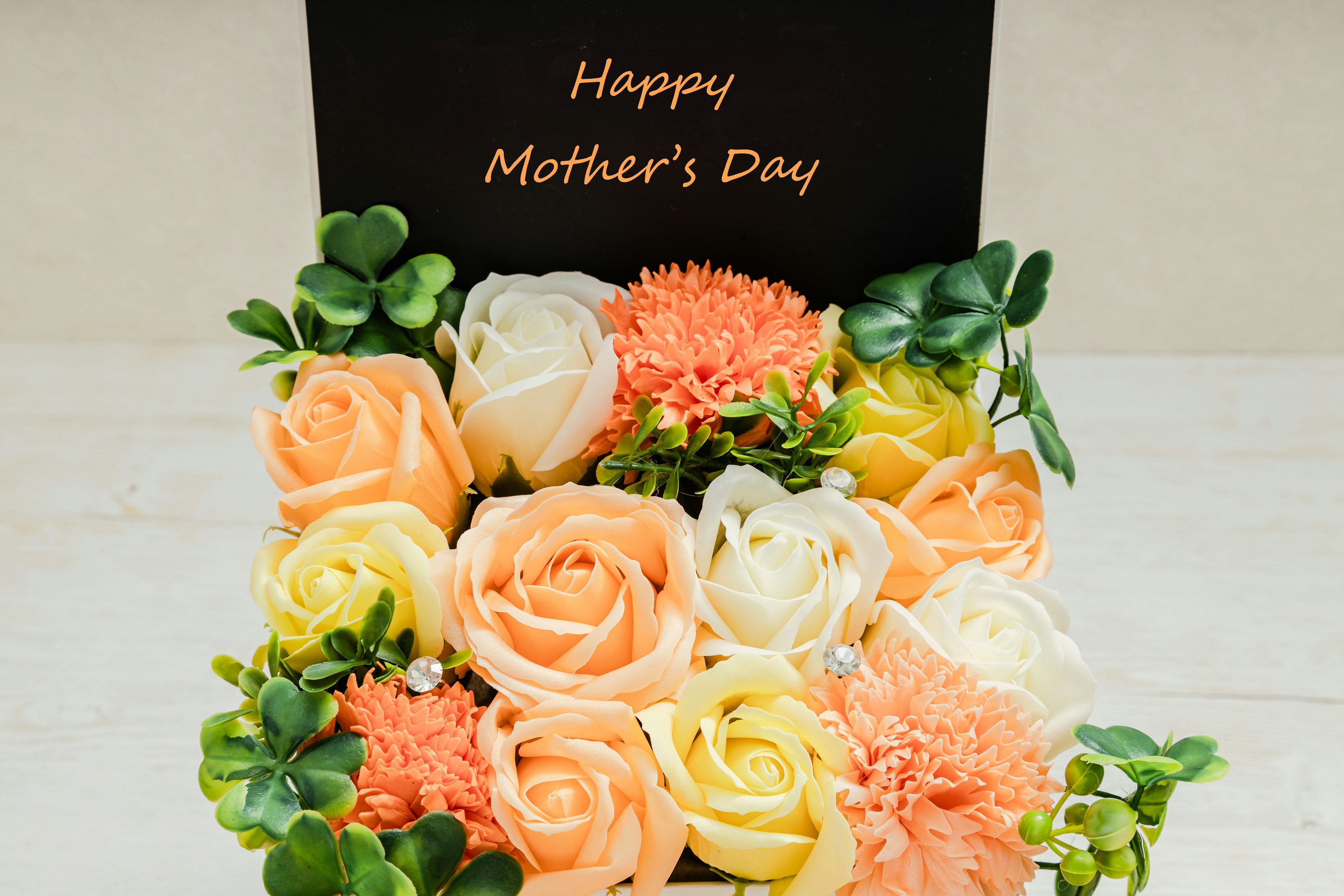 Arreglo floral con flores rosas, naranjas y blancas y una tarjeta negra que dice Feliz Día de la Madre