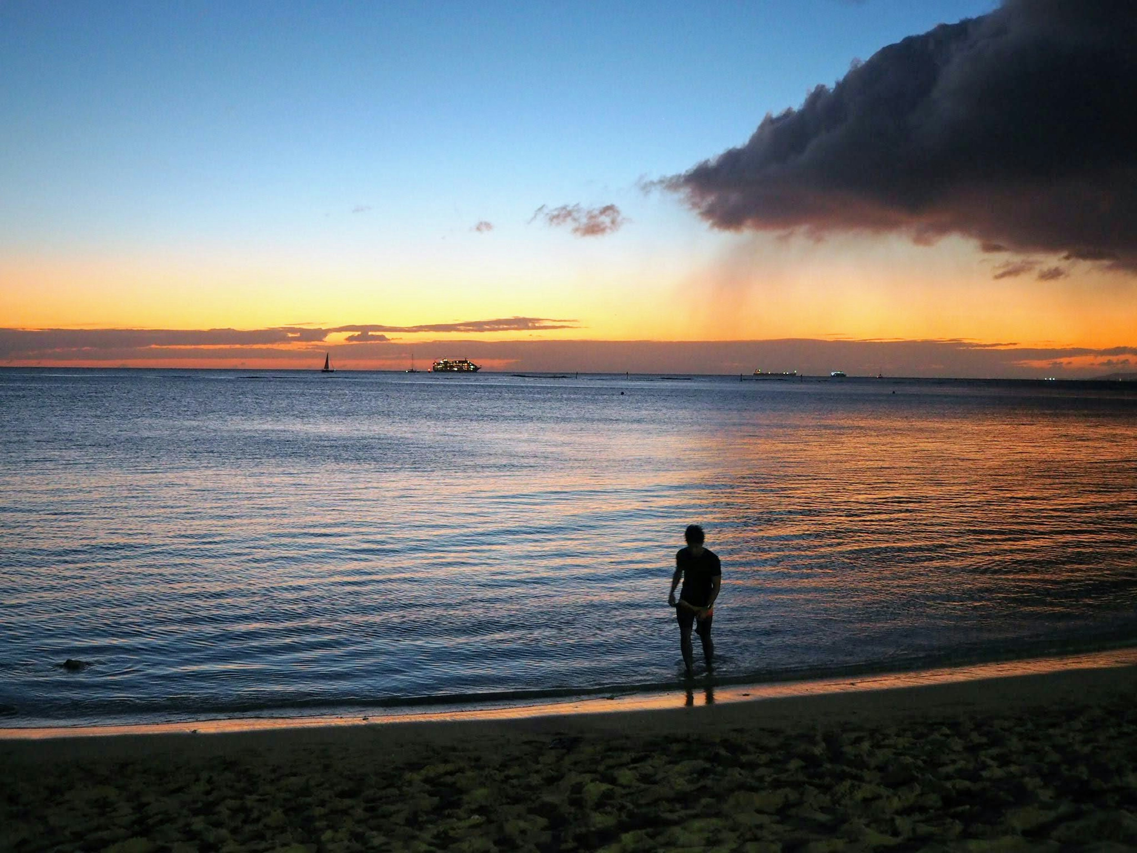 Silhouette einer Person, die am Strand mit einem Sonnenuntergang im Hintergrund steht